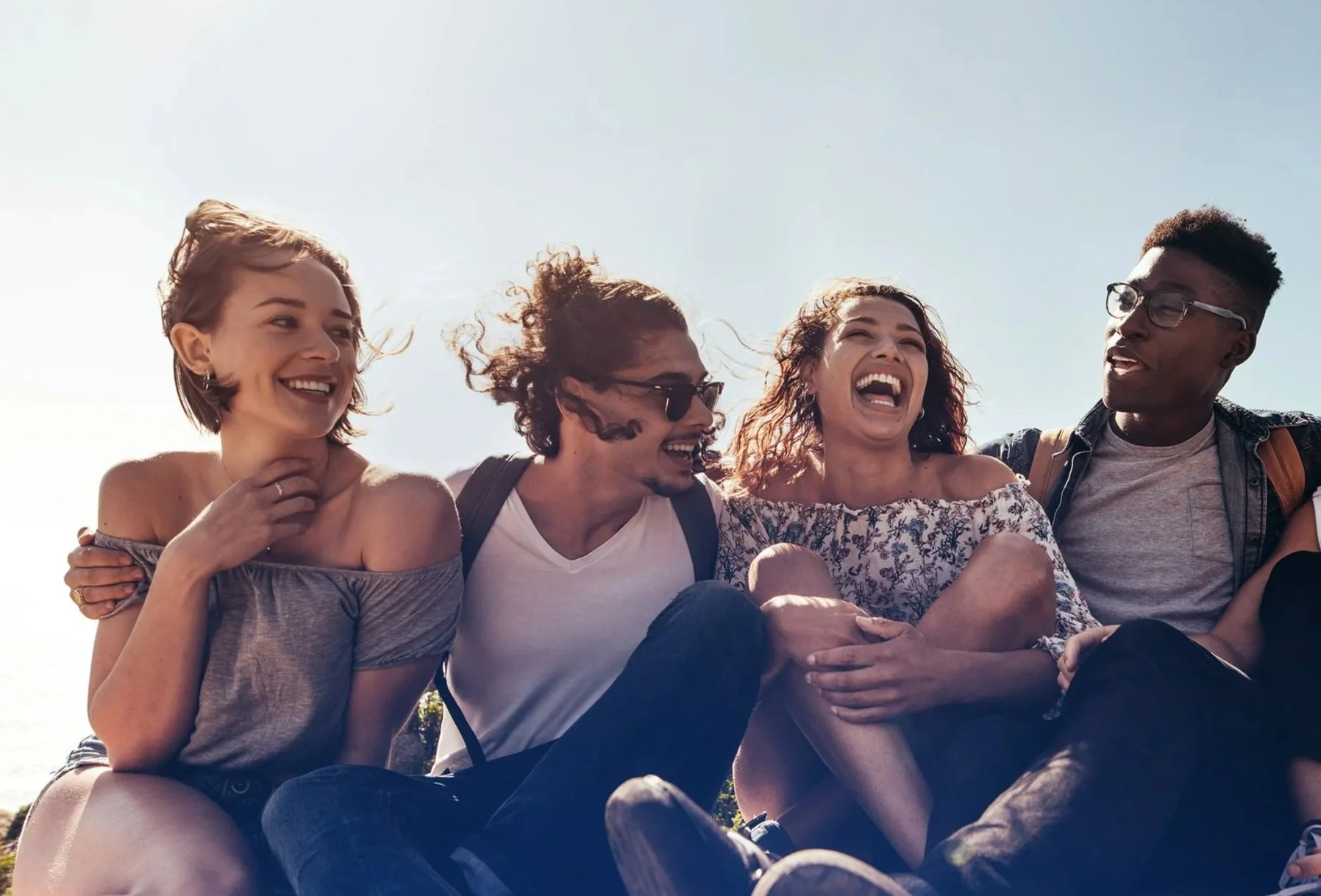 Four friends sitting outdoors laughing and enjoying each other's company on a sunny day.