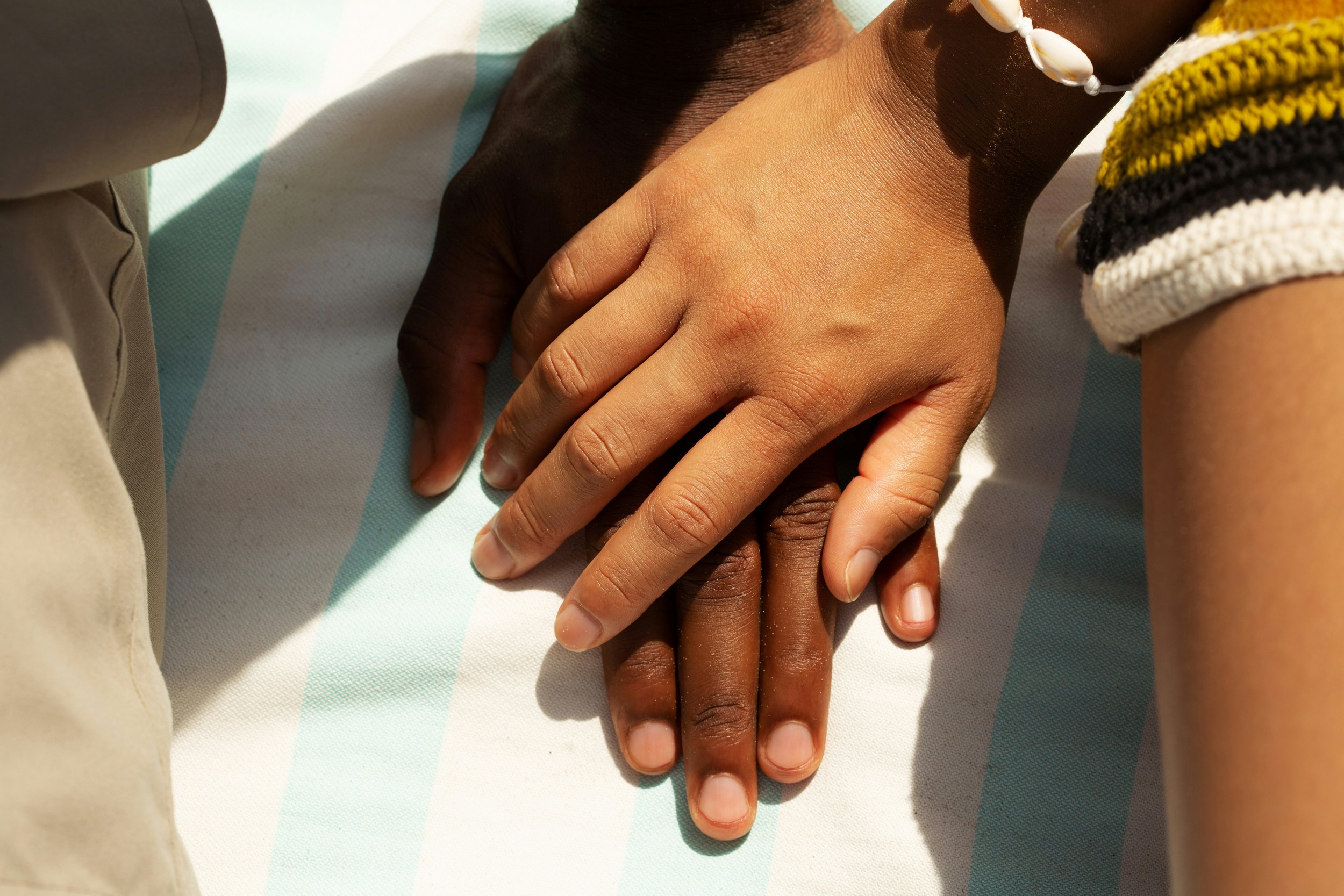 Close-up of two hands, one with darker skin and the other with lighter skin, gently clasped together on a white and light blue striped surface.