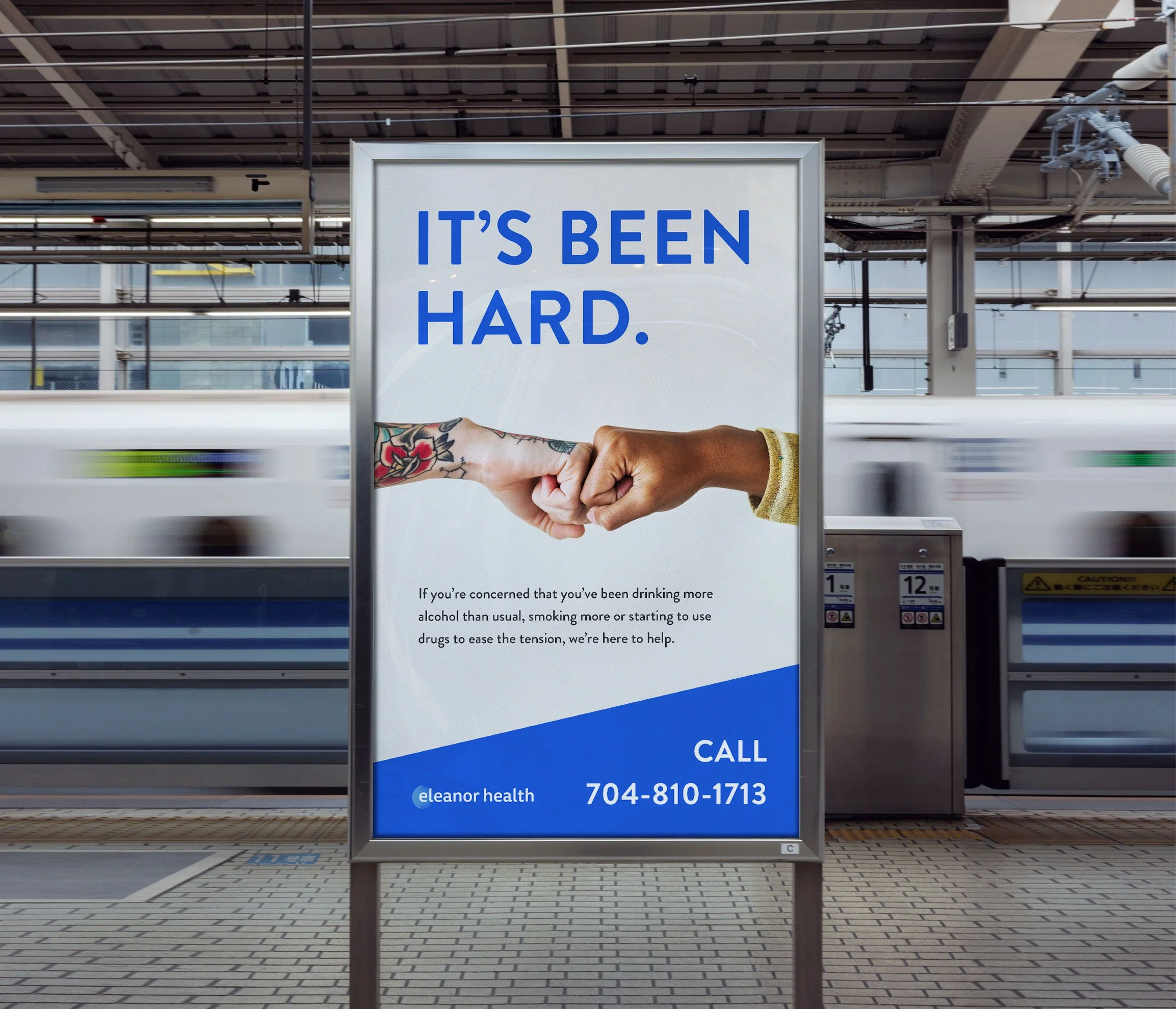 A train station platform features a poster with the text "IT'S BEEN HARD." showing a fist bump between two people, one with a tattooed arm. Below, there is information about mental health support, including a phone number for Eleanor Health.