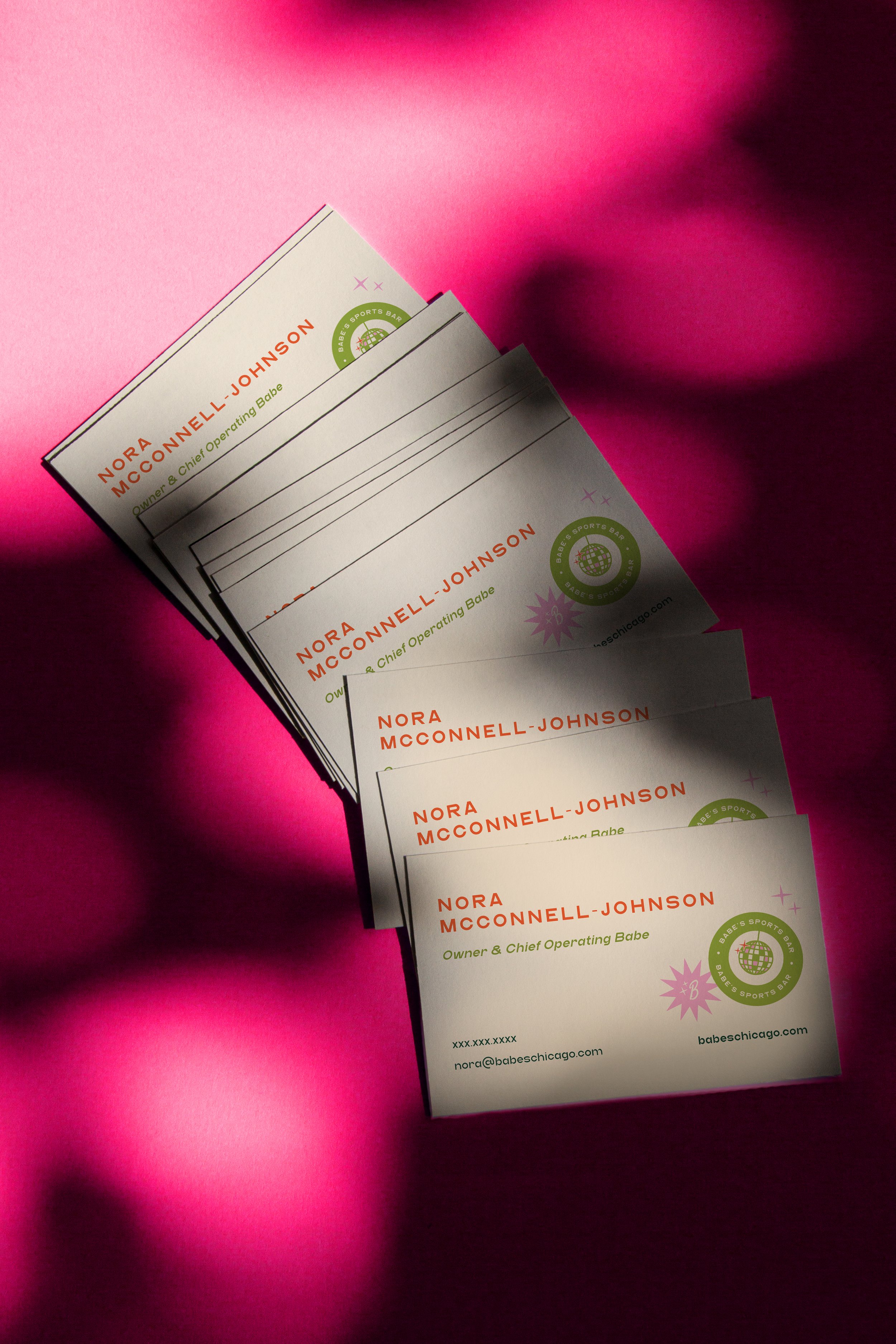 Business cards stacked on a pink surface with shadows cast across them.