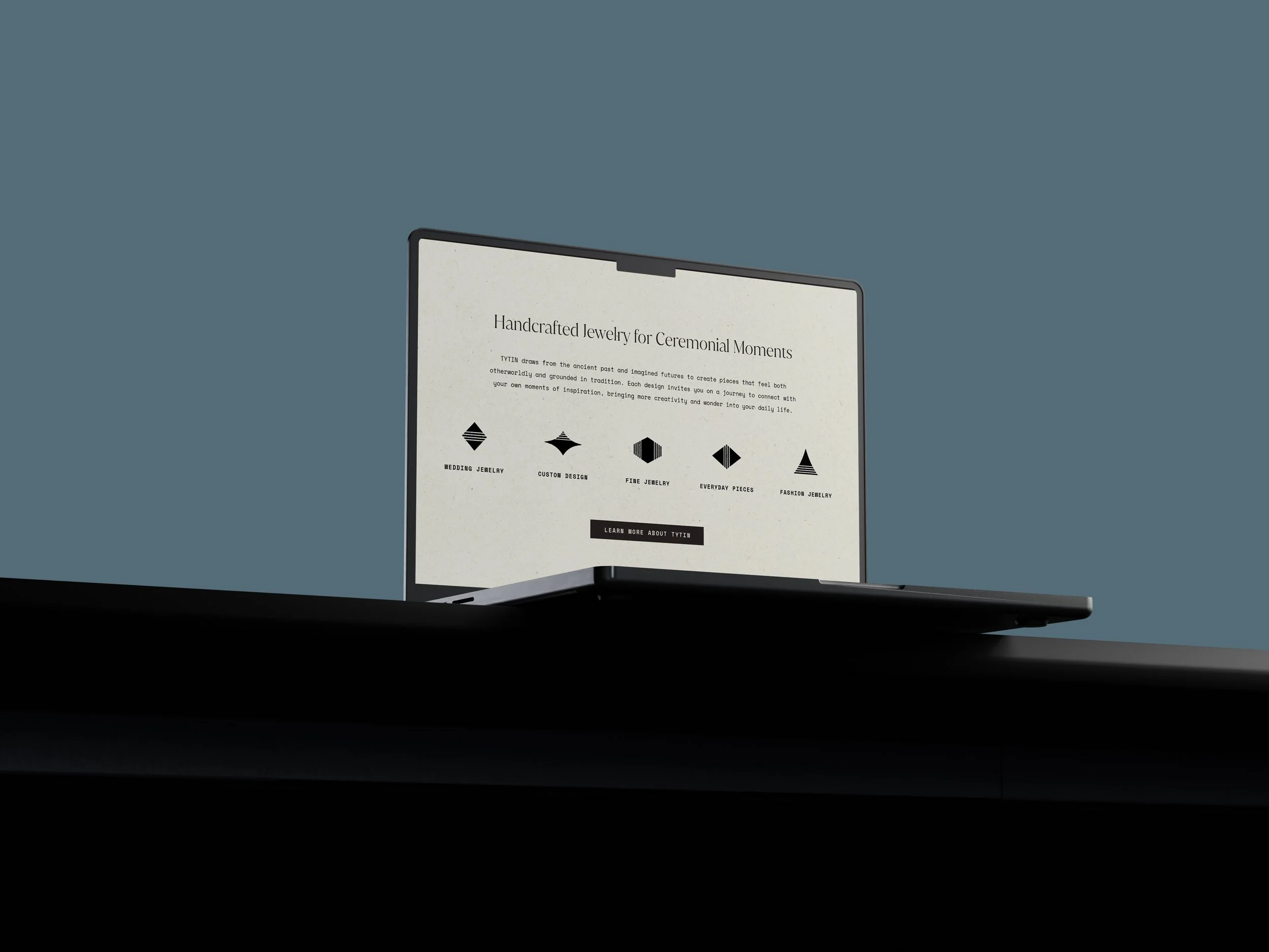A laptop on a black surface displaying a webpage about handcrafted jewelry for ceremonial moments, with text and five icons representing different jewelry categories.