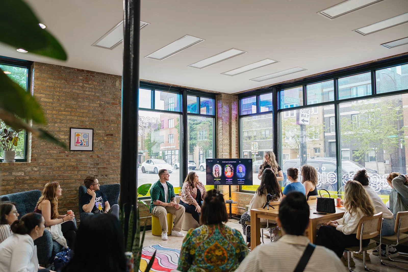 A group of people attending a presentation at Magic Eight Co.'s studio. A woman is standing near a screen displaying profiles, speaking to the seated audience.