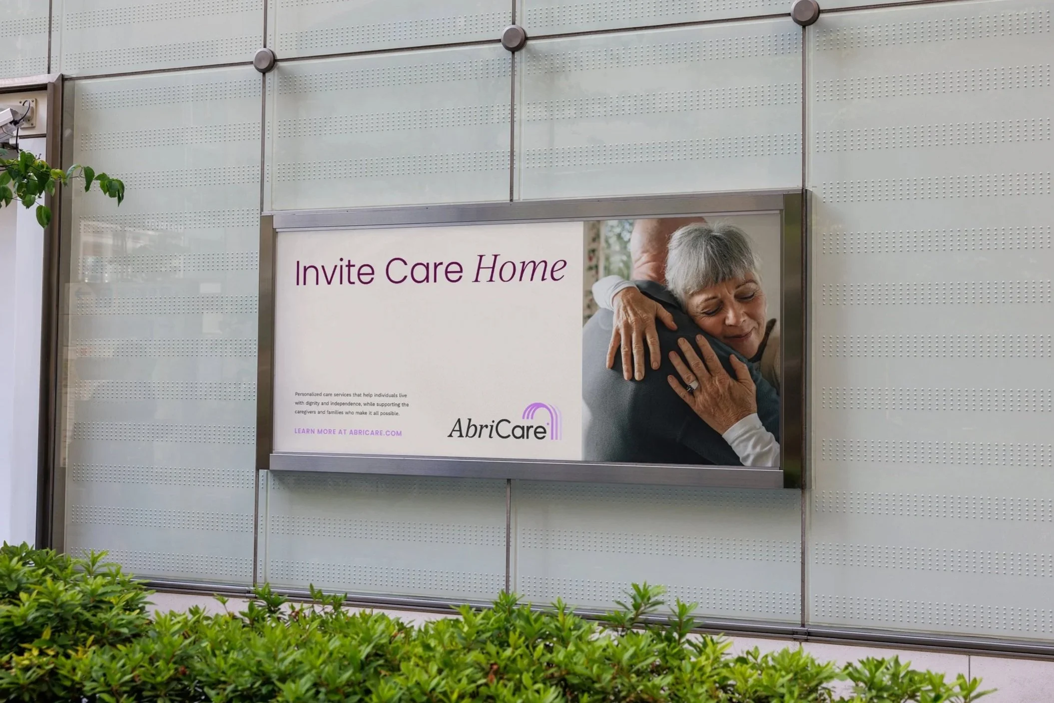 A large advertisement for AbriCare on an exterior wall, featuring a woman hugging someone, with text inviting people to care home services.