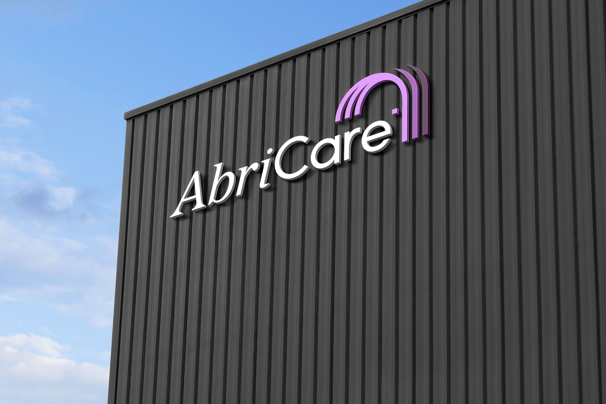 A building with a sign that reads 'AbriCare' along with a purple logo resembling a stylized rainbow or arc, against a partly cloudy sky.