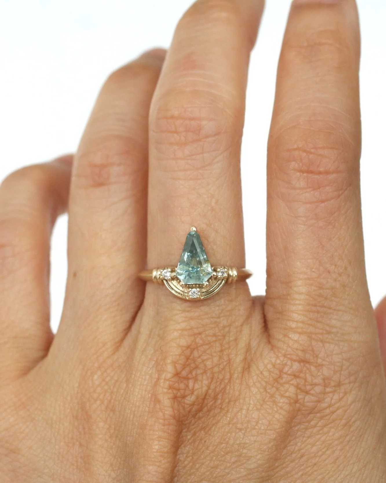 A person's hand displaying a gold ring with a large pear-shaped blue gemstone and small diamonds surrounding it.