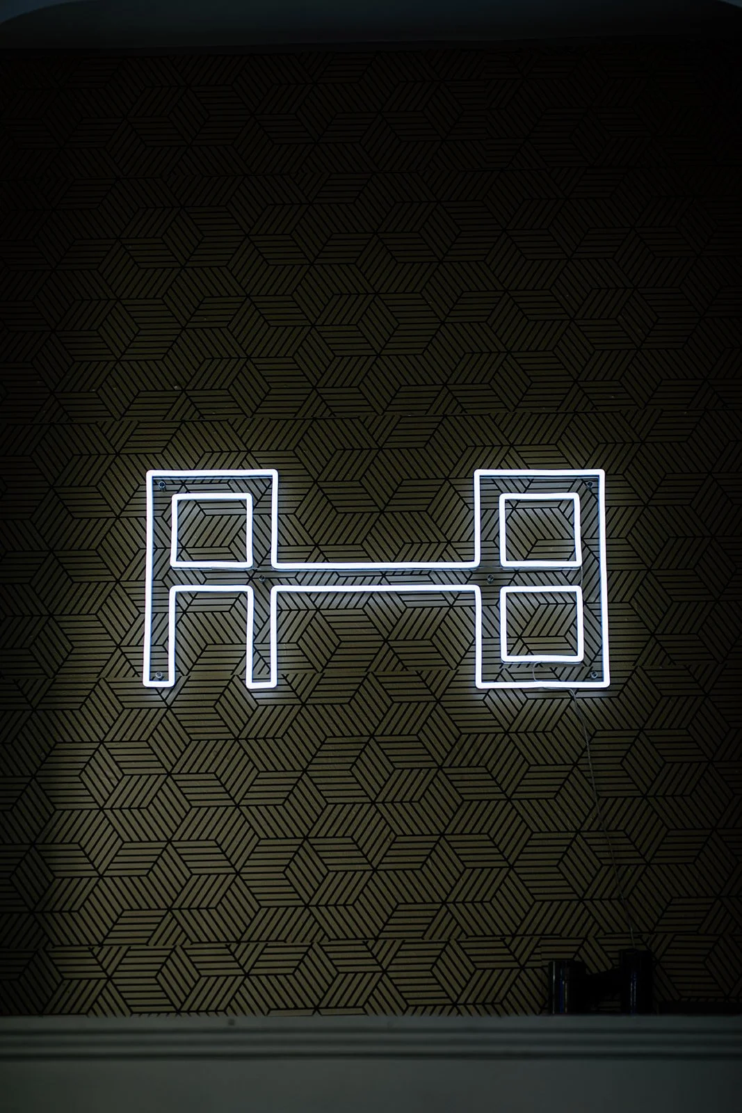 Neon light art on a wall with Above the Bar's logomark.