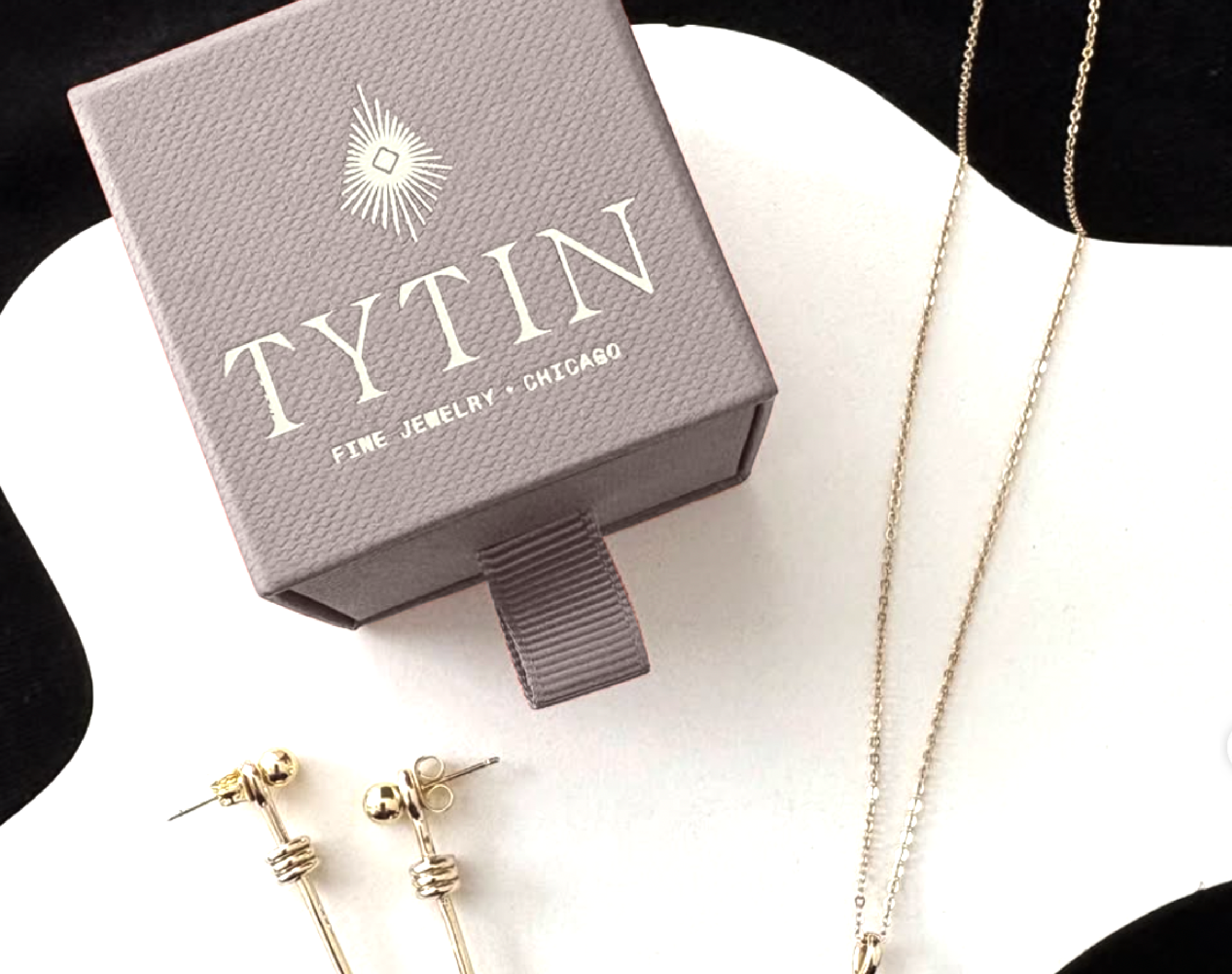 Gold jewelry including earrings and chains on a white display surface, with a gray box labeled "Tytin" in the background.
