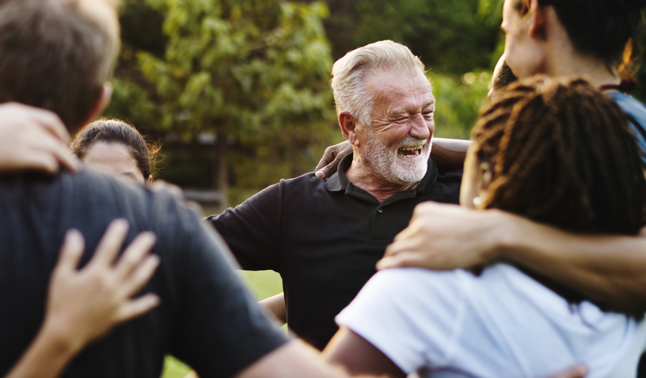Group of people embracing outdoors, smiling, and laughing.