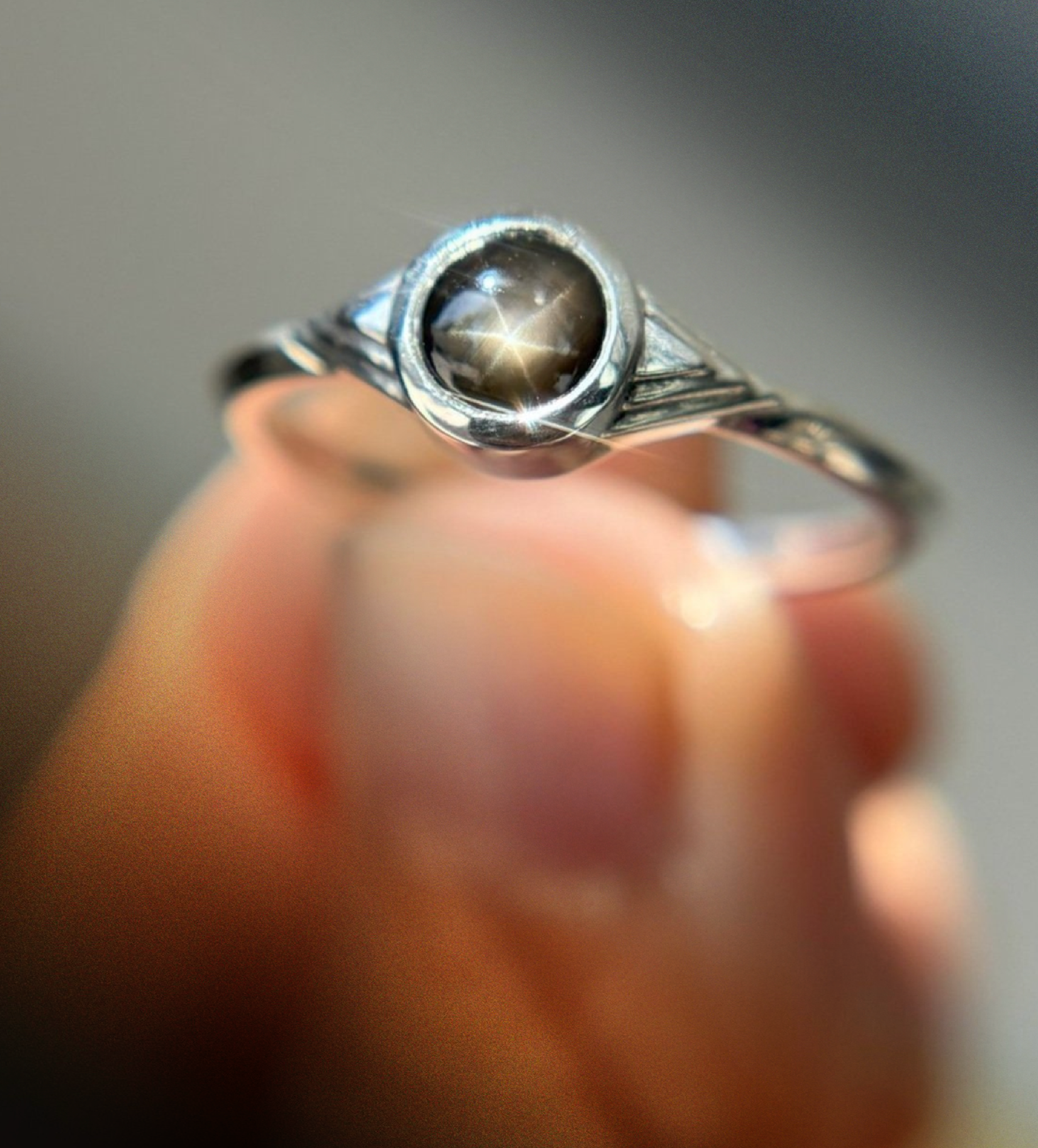 Close-up of a silver ring with a dark gemstone, held between fingers.