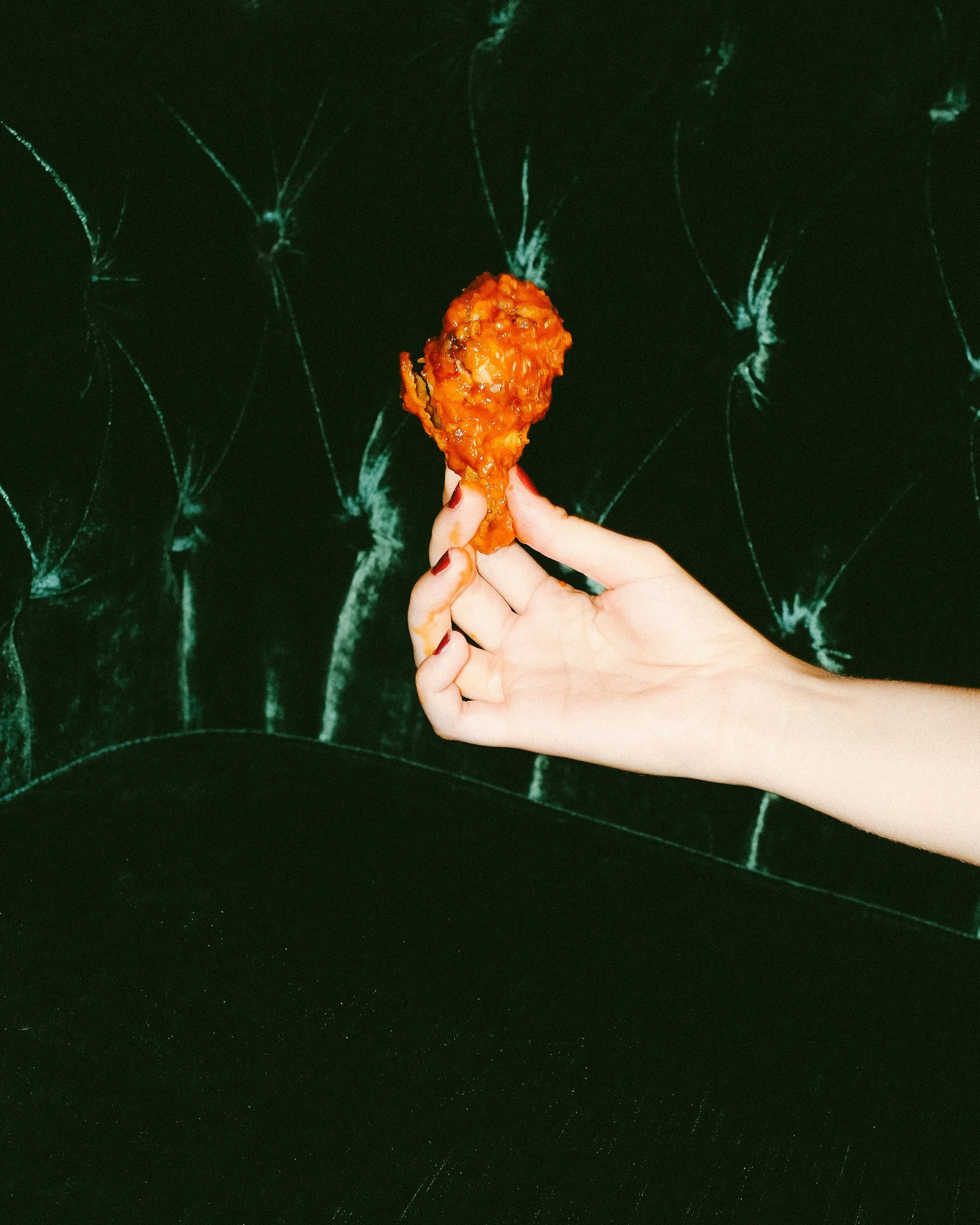 Hand holding a piece of fried chicken against a dark, textured background.