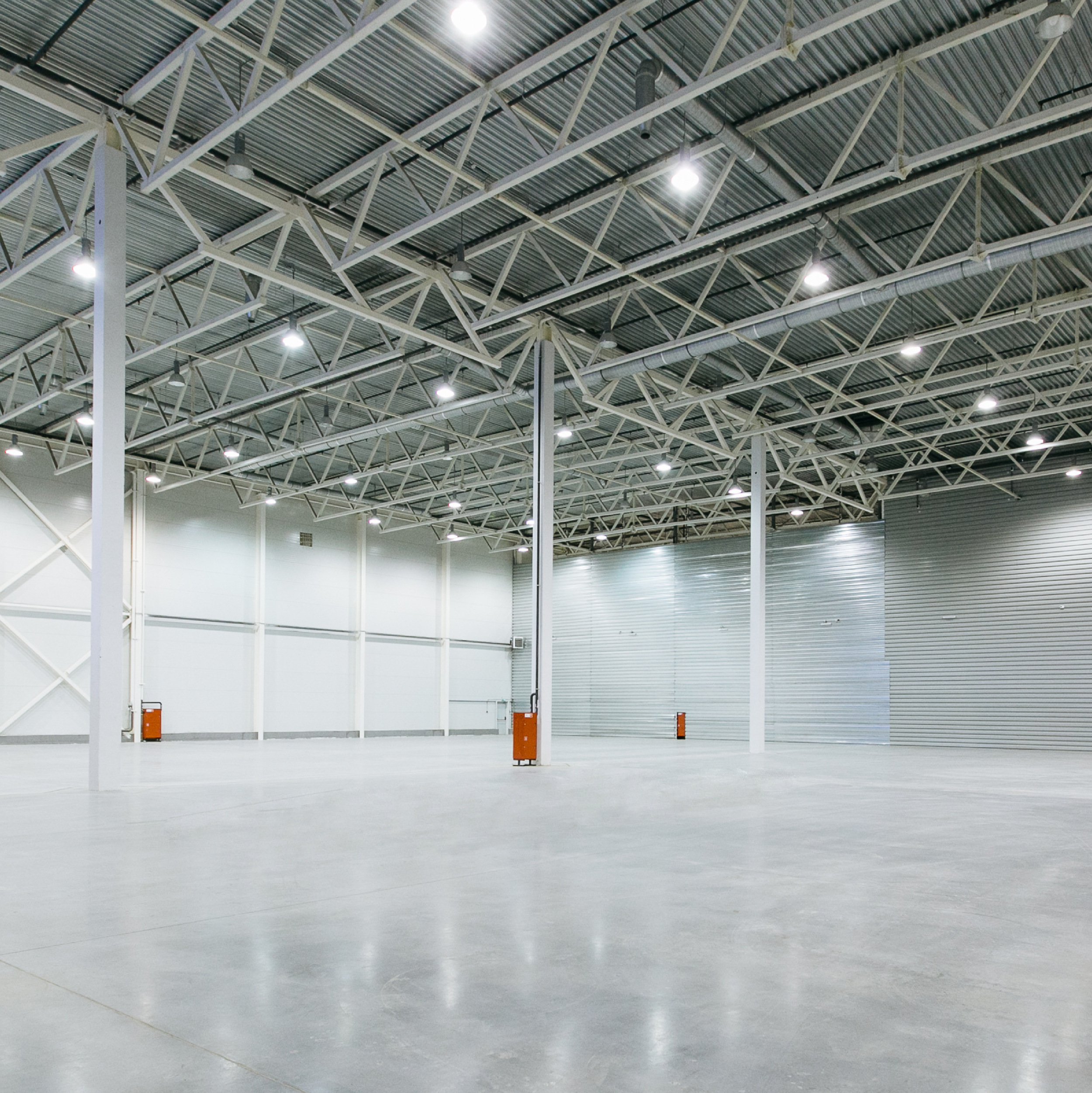Empty warehouse with high ceiling, metal beams, and bright lighting.