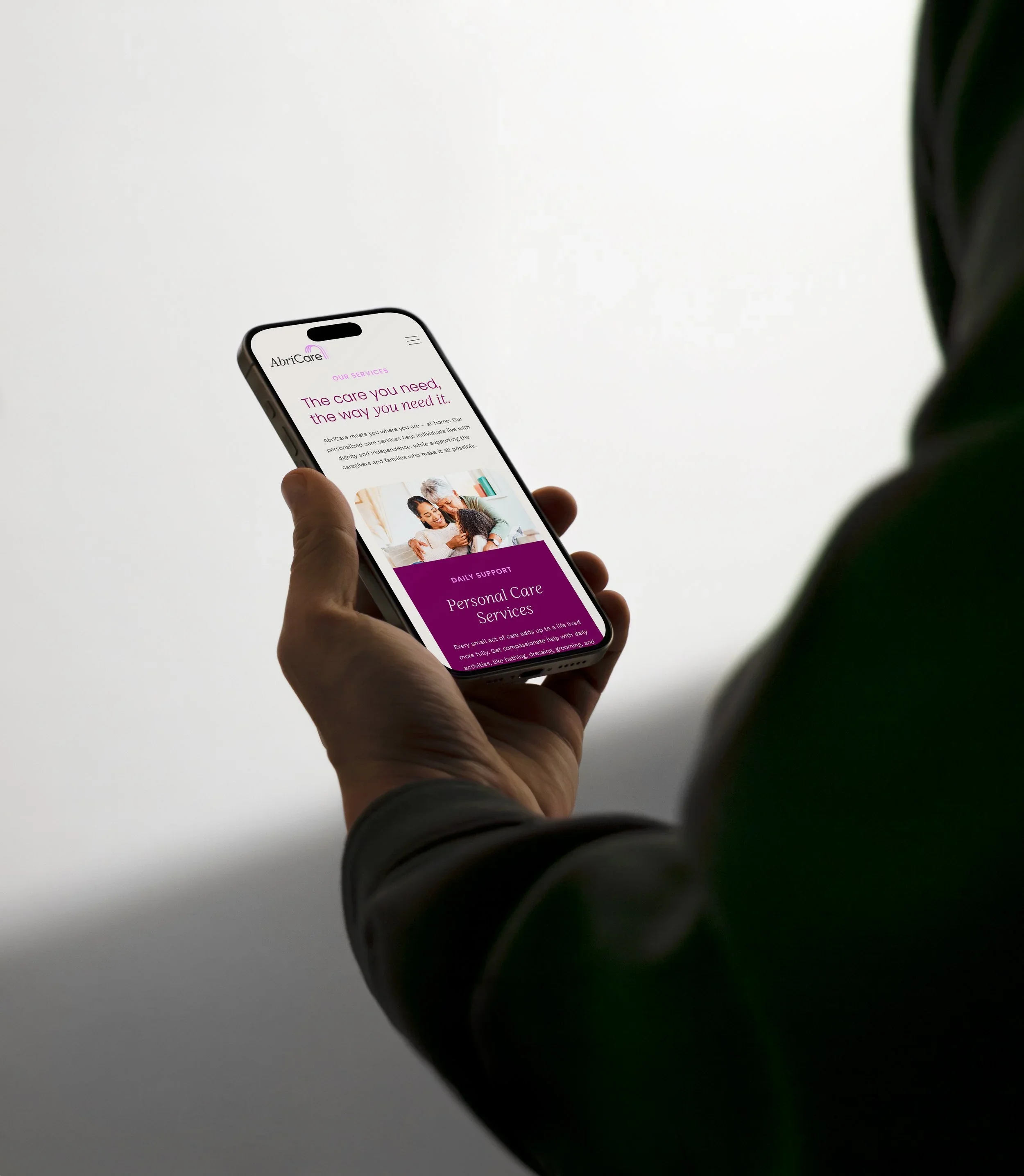 Person holding a smartphone displaying a healthcare service webpage, with a focus on personal care services and support, in front of a plain white background.