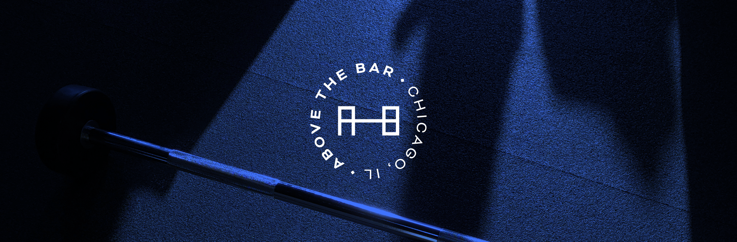 A close-up view of a dark textured surface with a golf club shaft and a circular logo of a barbell with the text 'ABOVE THE BAR · CHICAGO, IL' illuminated on the surface.