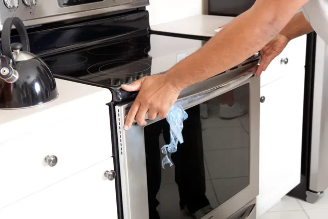 Person removing or cleaning the oven door of an electric stove in a kitchen.