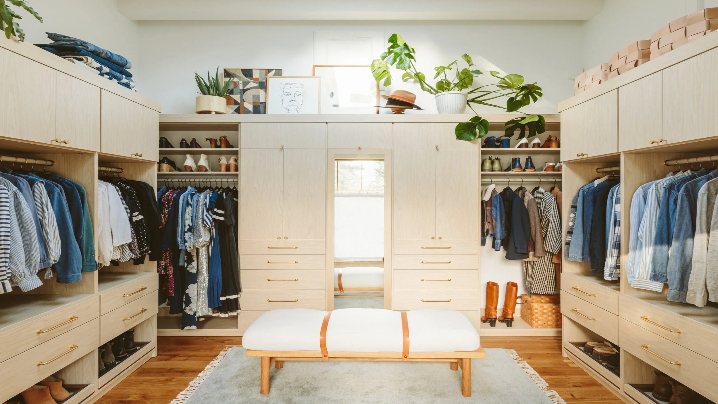 Walk-in closet with organized clothing, shoes, and accessories, decorated with plants and artwork.