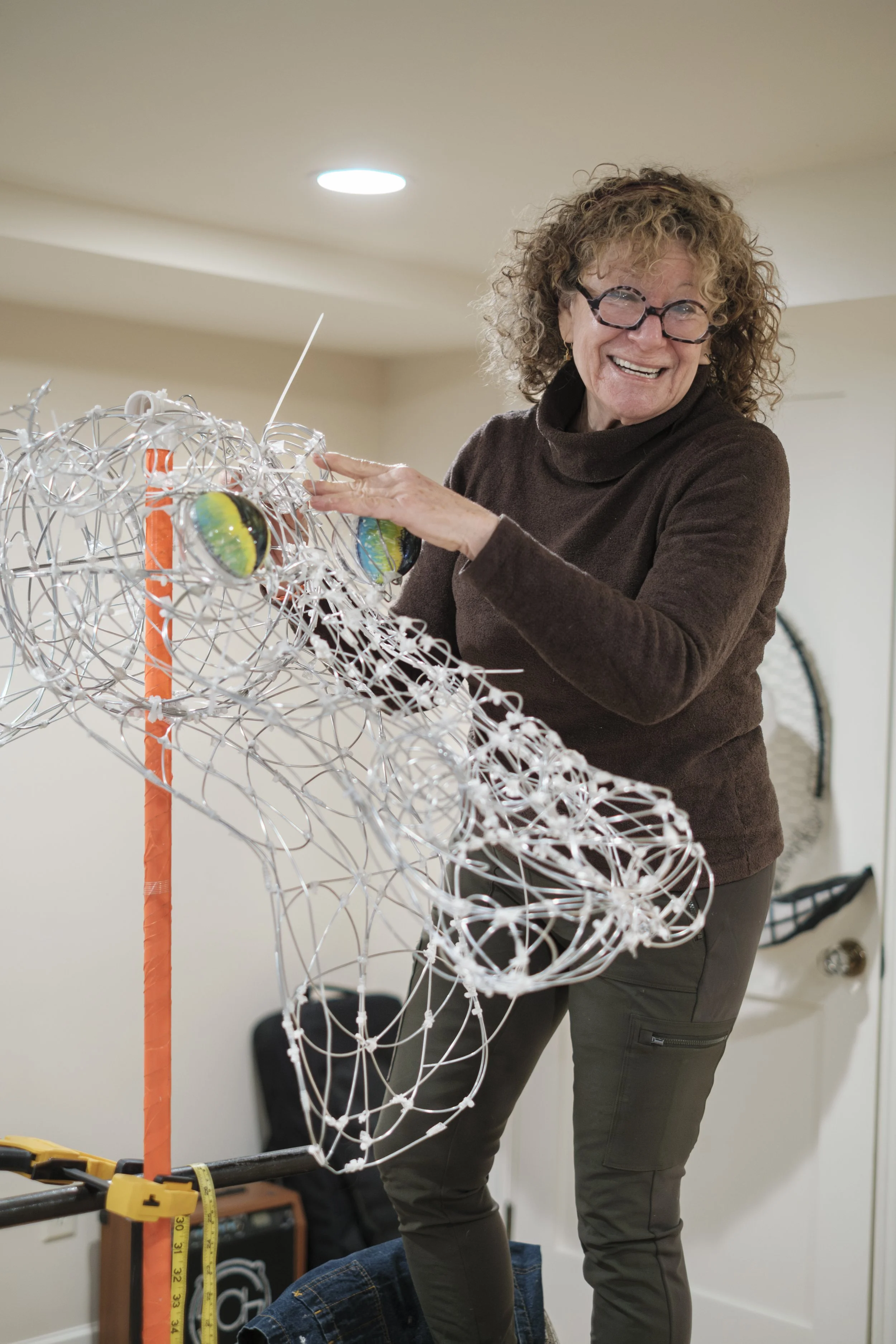 Artist Jeri Rosenberg smiles while bending metal onto a metal dragon sculpture.