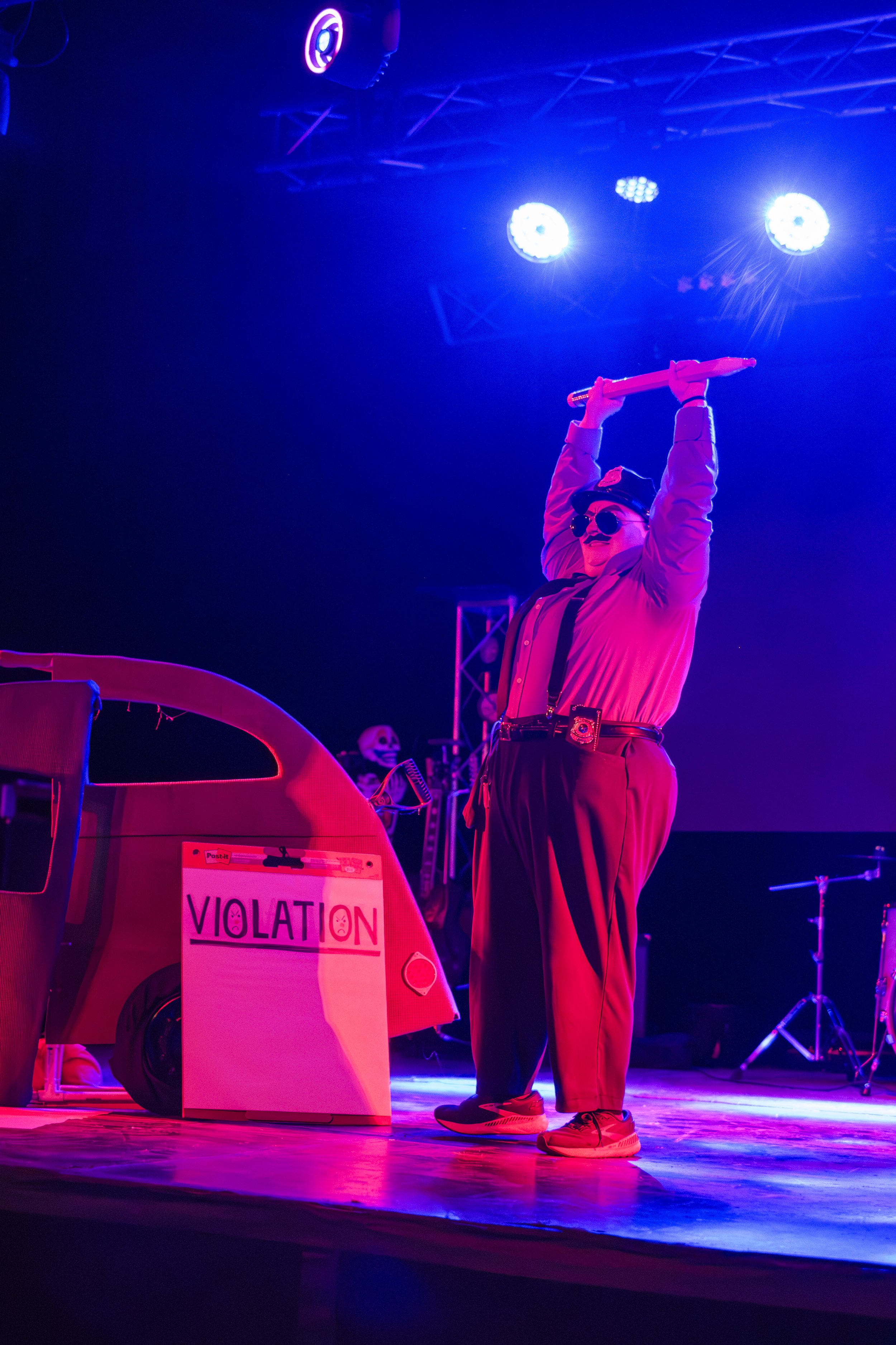 Clown wrestler Bert Simmons holds a large pencil over their head while standing next to a large notepad that reads "violation".