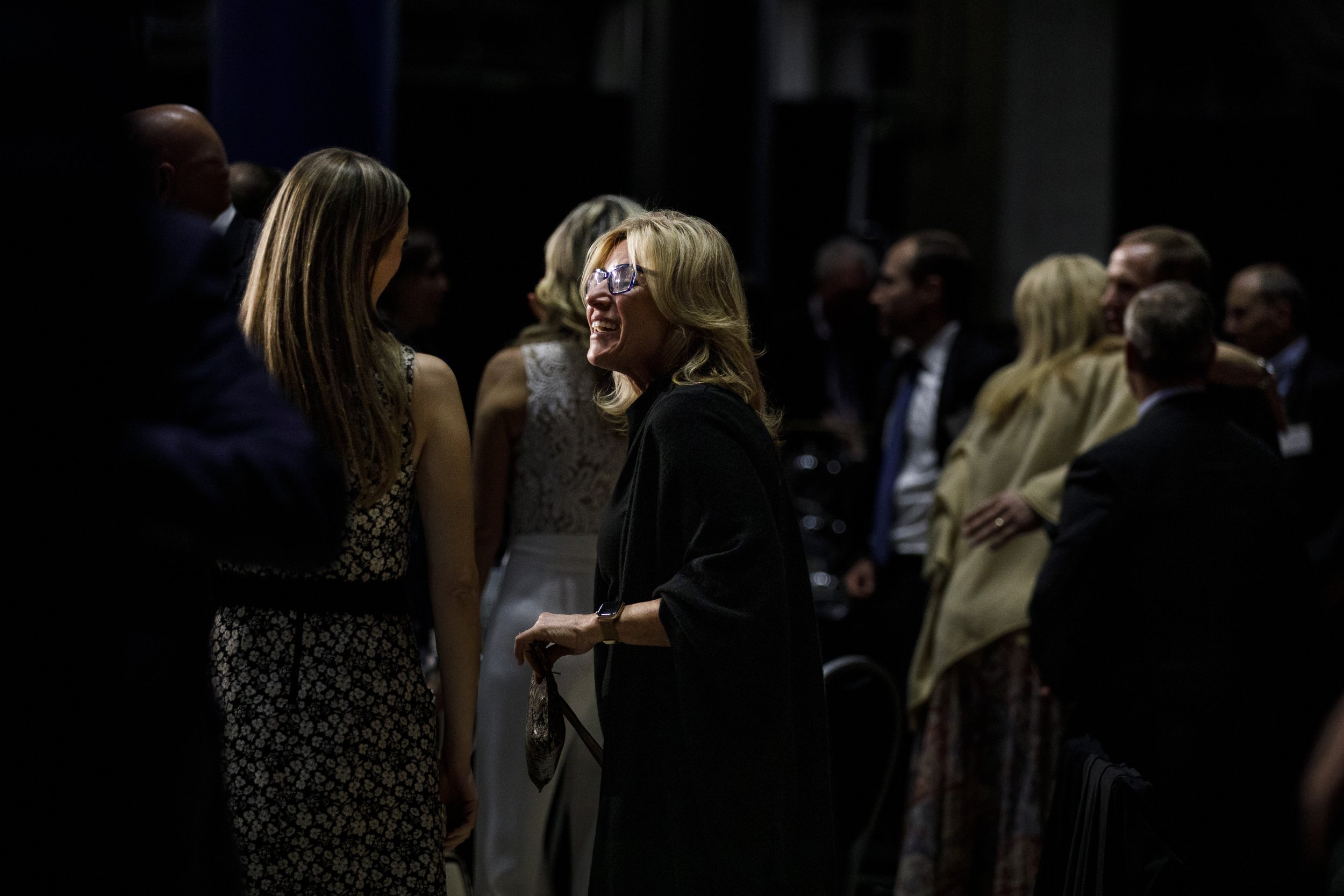 A woman is partially illuminated while smiling and talking to another woman.