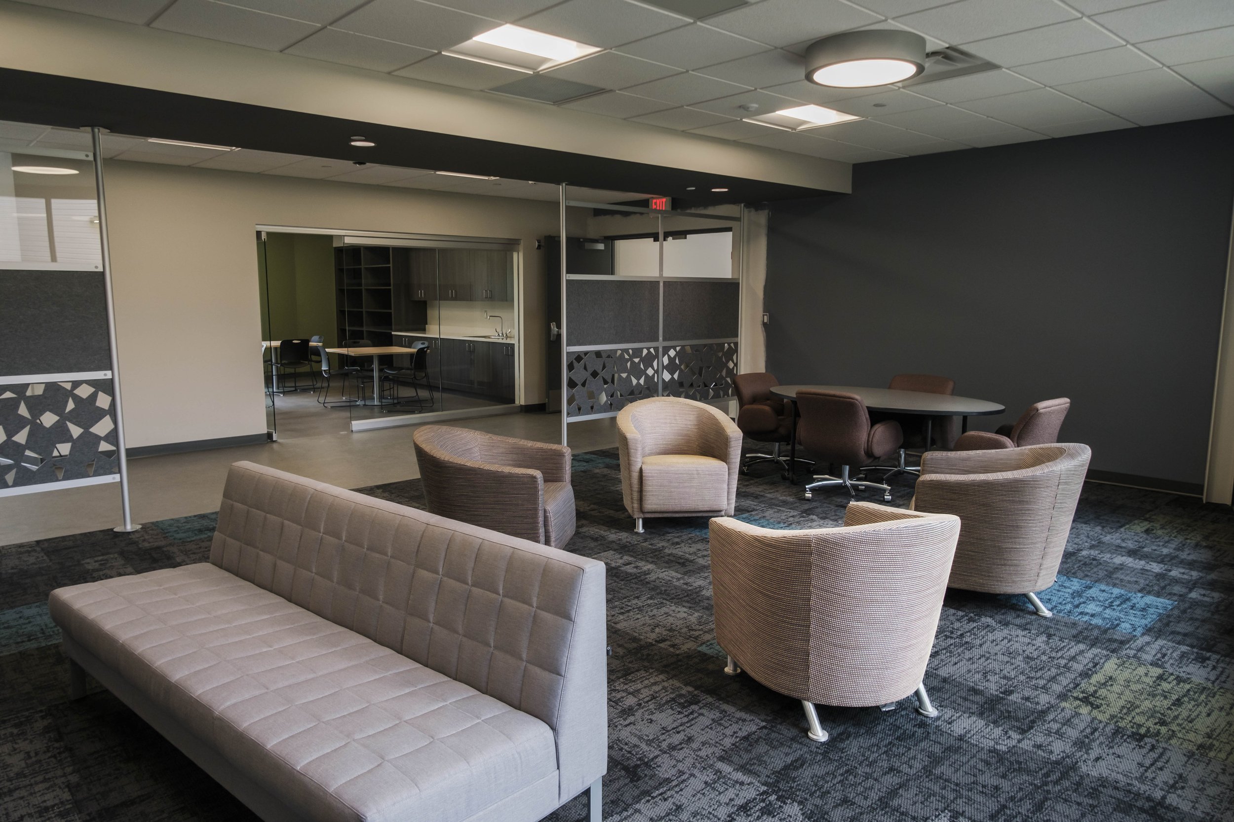 A bright indoor space with multiple chairs, a couch and multi colored carpet.