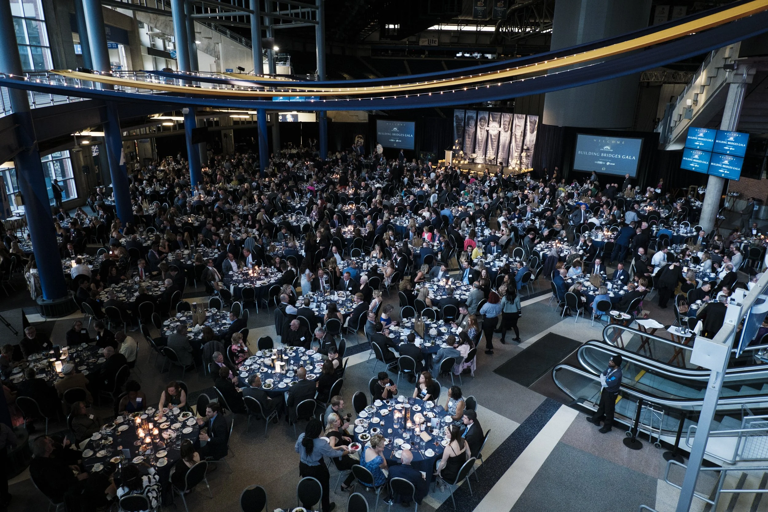 An elevated view of over twenty tables with seats neatly set up with people standing around them.