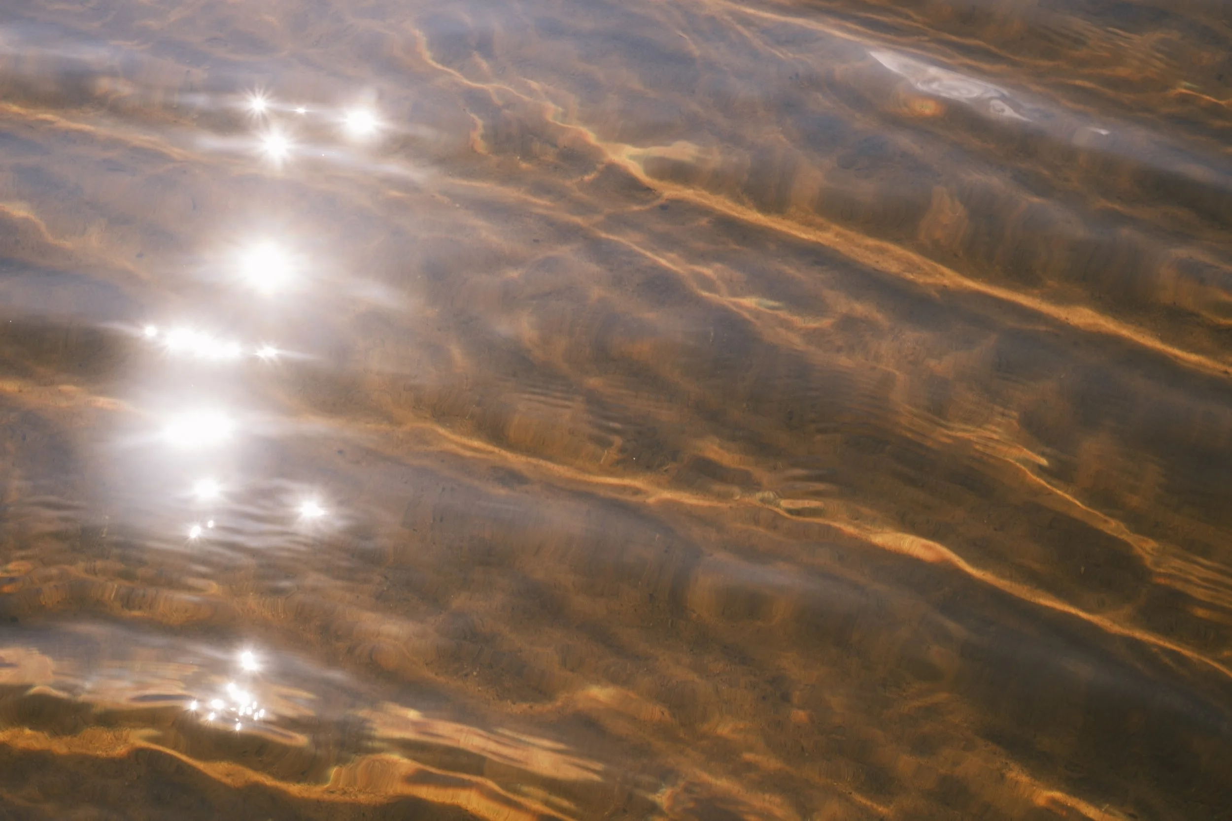 Sun light is reflected on the surface of water, with the light from the ripples are cast on the bottom of a lake.