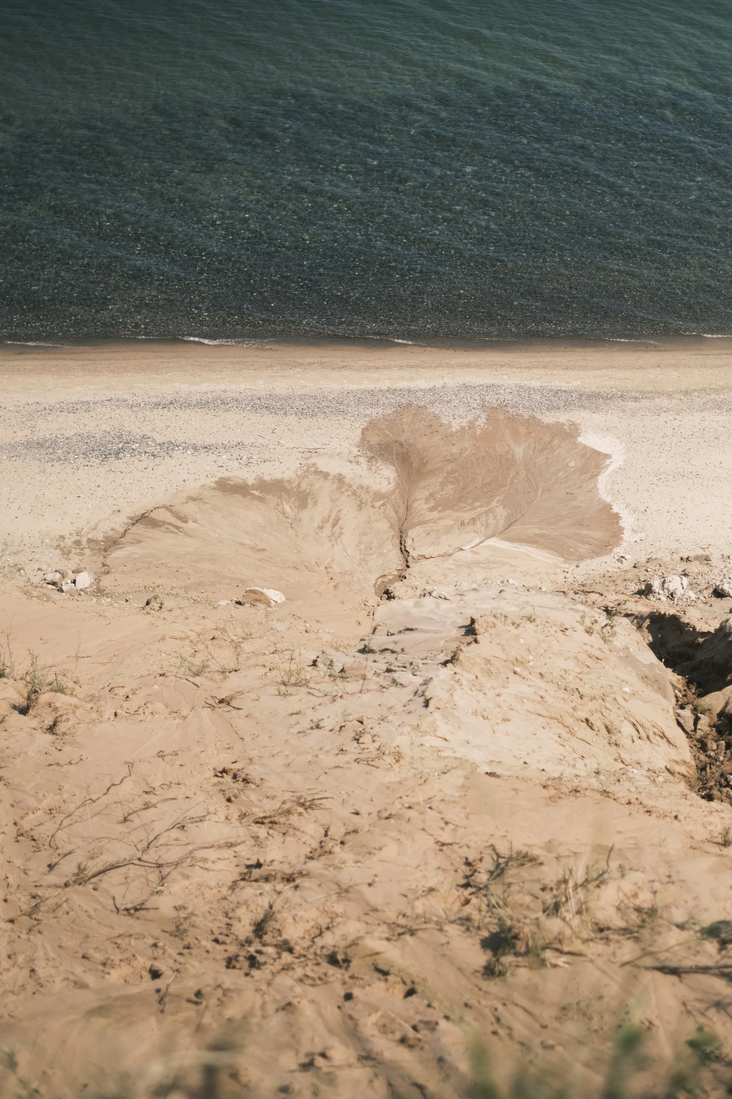 A bird's eye view of light brown, naturally occuring clay splays out from a crevice in a from a sand dune on a beach.