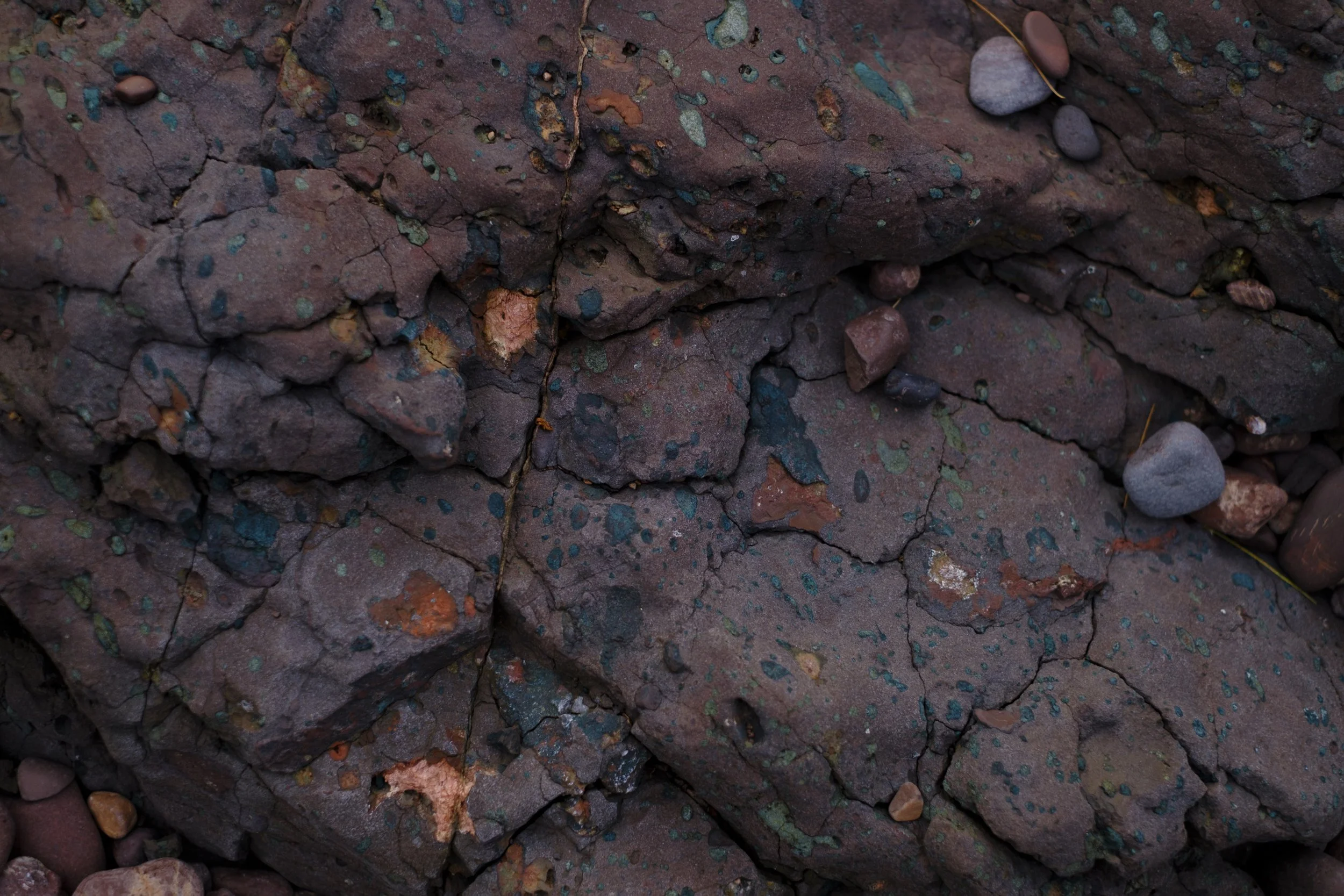 A close up of small, earth-toned orange and blue stones sit atop a larger, reddish brown rock.