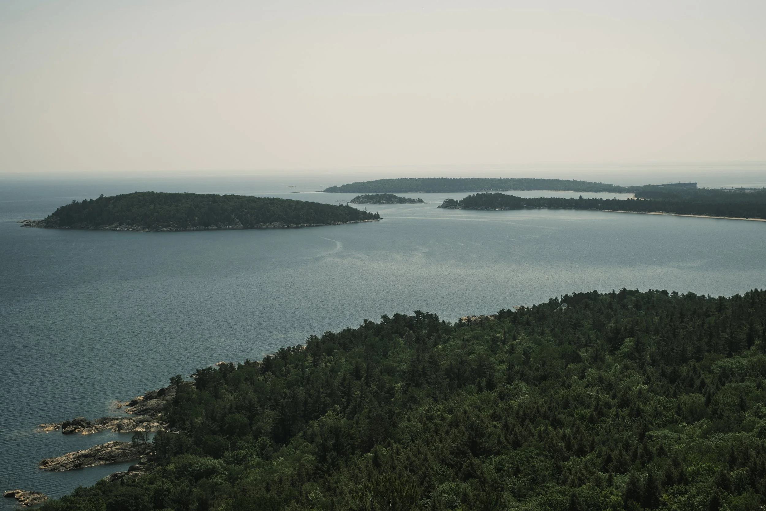 A mile high perspective of small, unhabited, tree covered islands in Lake Superior against a hazy, gray sky. is