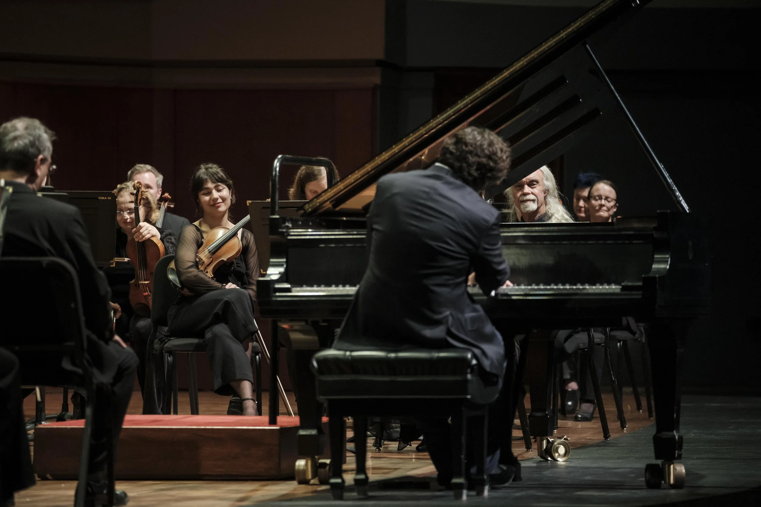 Musicians onstage, framed through the piano, as Martin James Bartlett plays a solo.