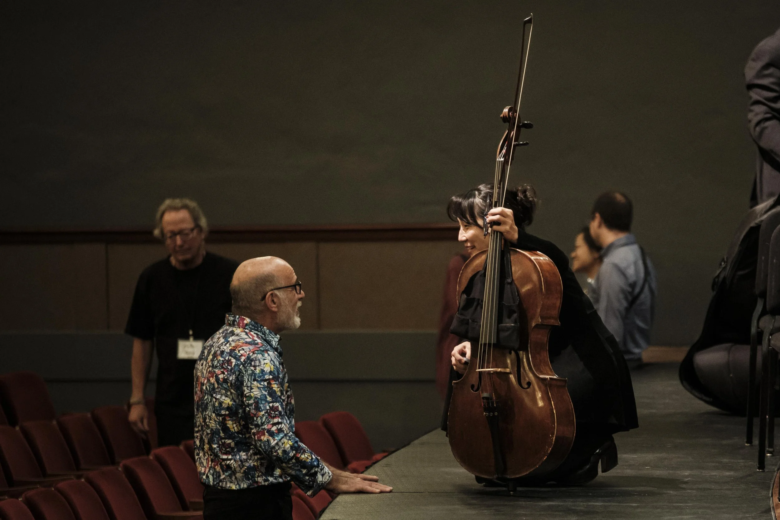 Audience member talks with a musician who is kneeling on stage after a concert.