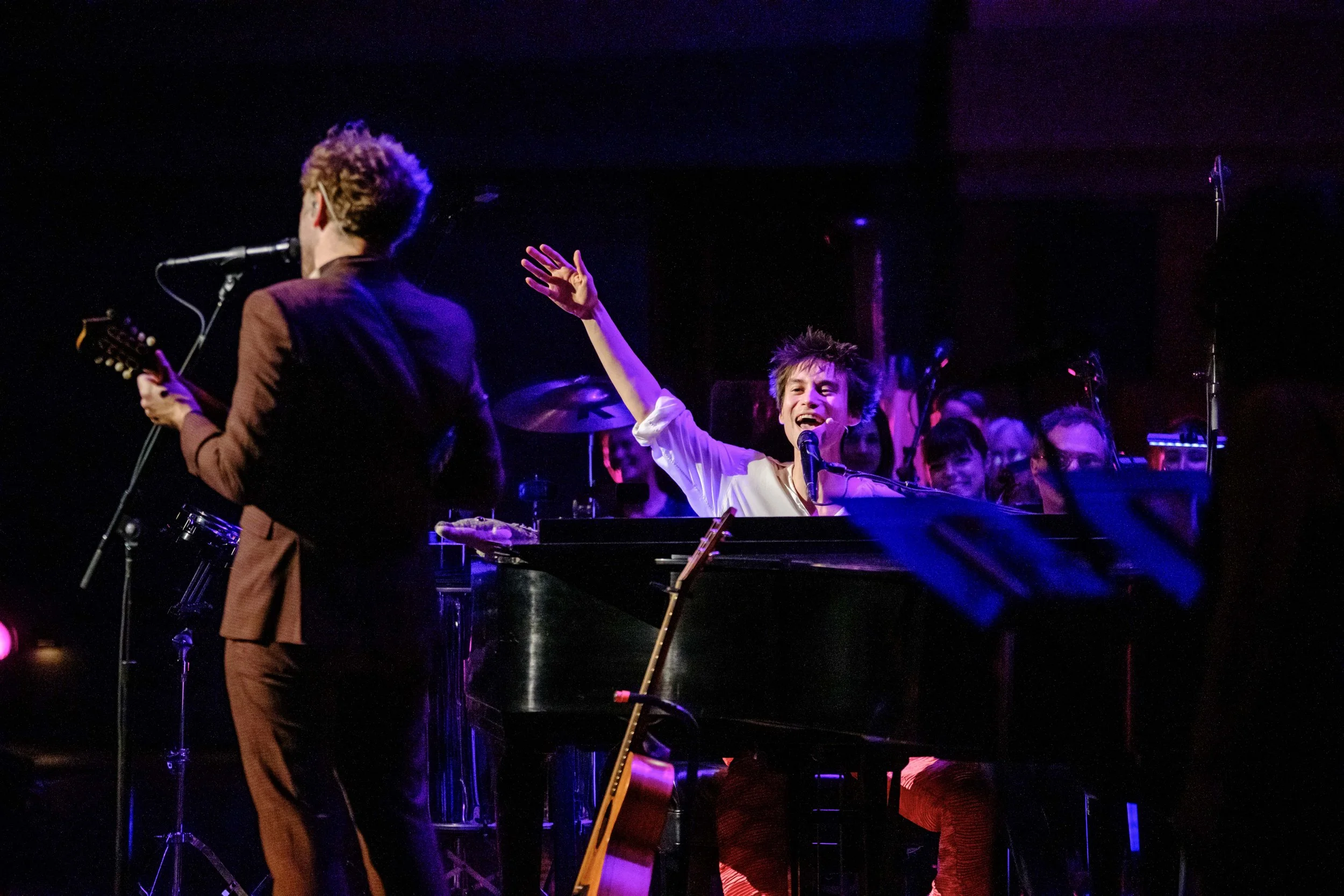 Jacob Collier singing onstage with a piano during a concert with the Ann Arbor Symphony Orchestra and Chris Thile.