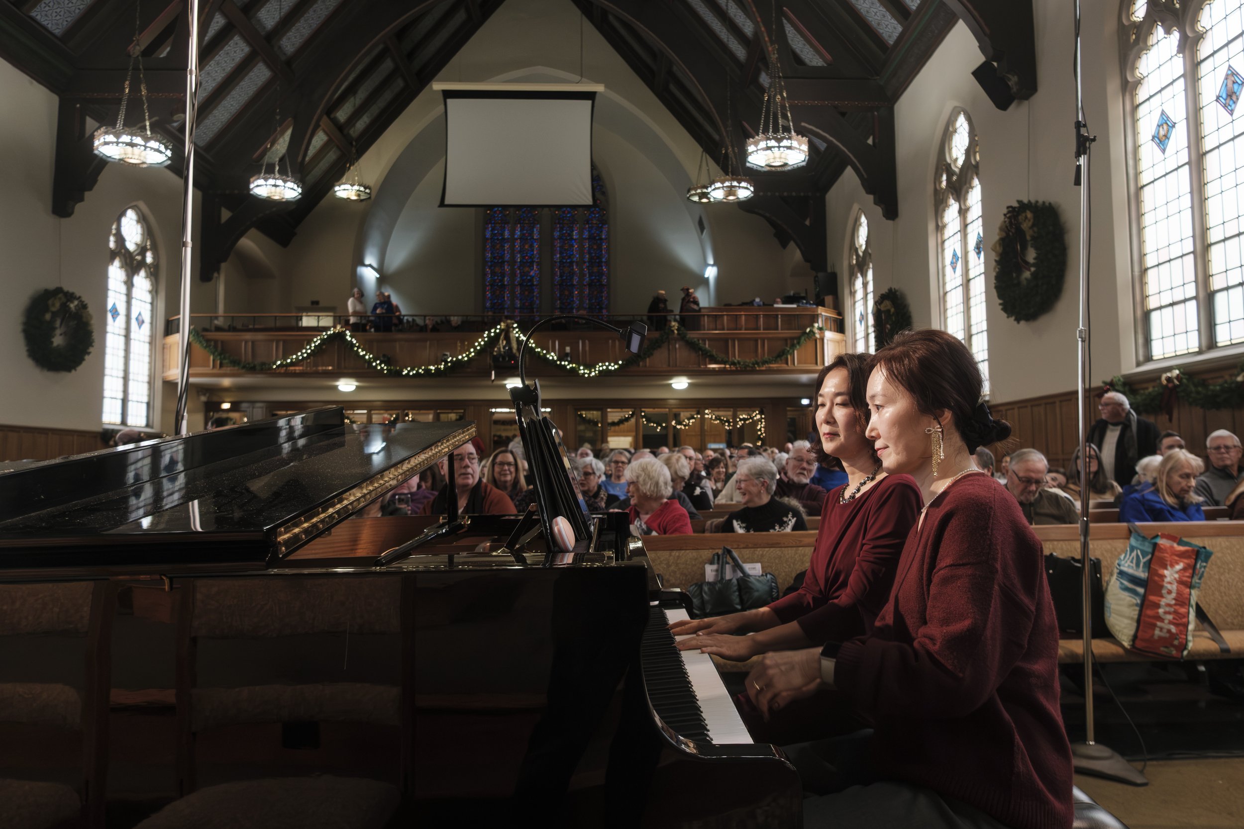 Two piano players play on stage at the First United Methodist Church of Ann Arbor while the audience filters in