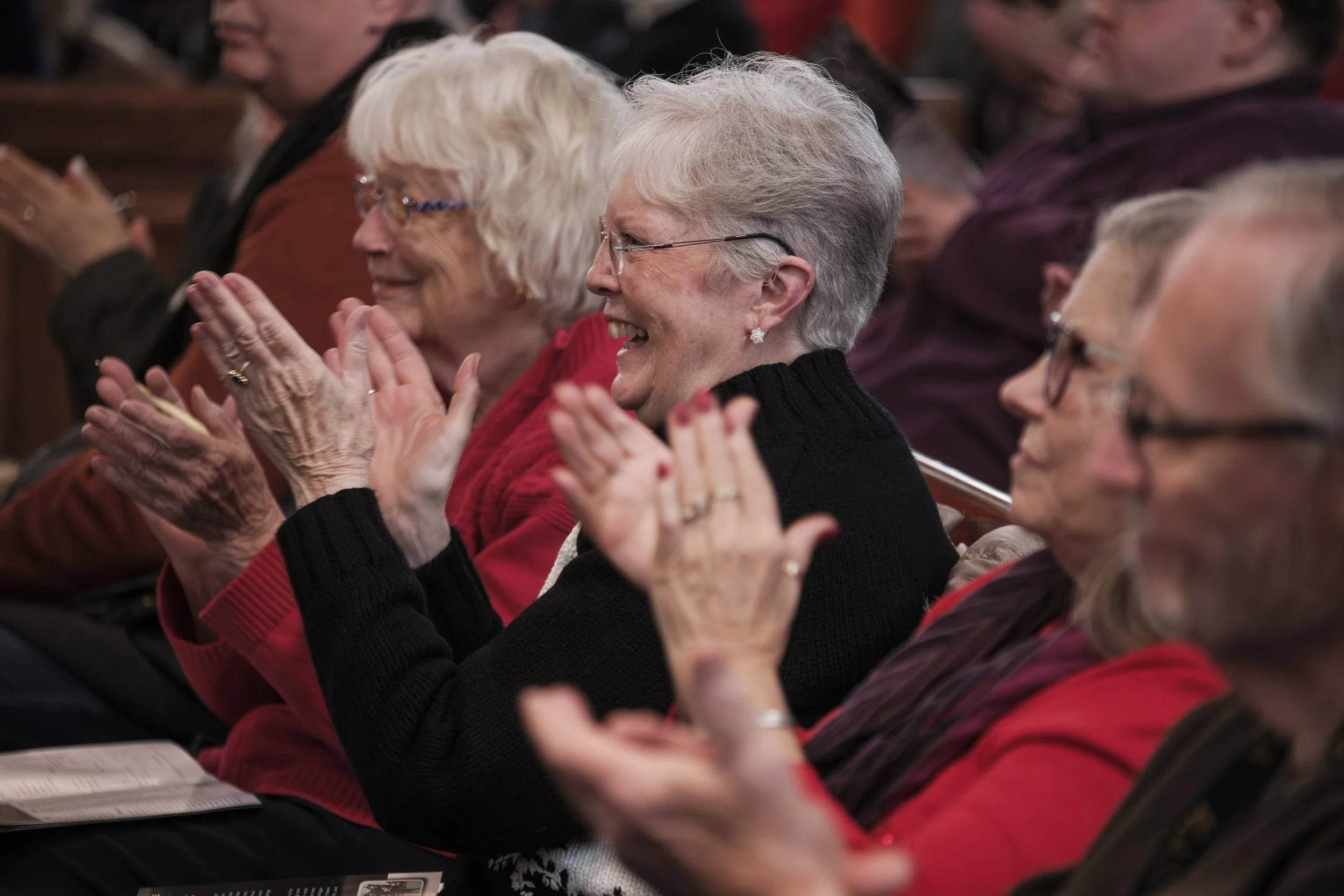 Three older women with glasses smile and clap.