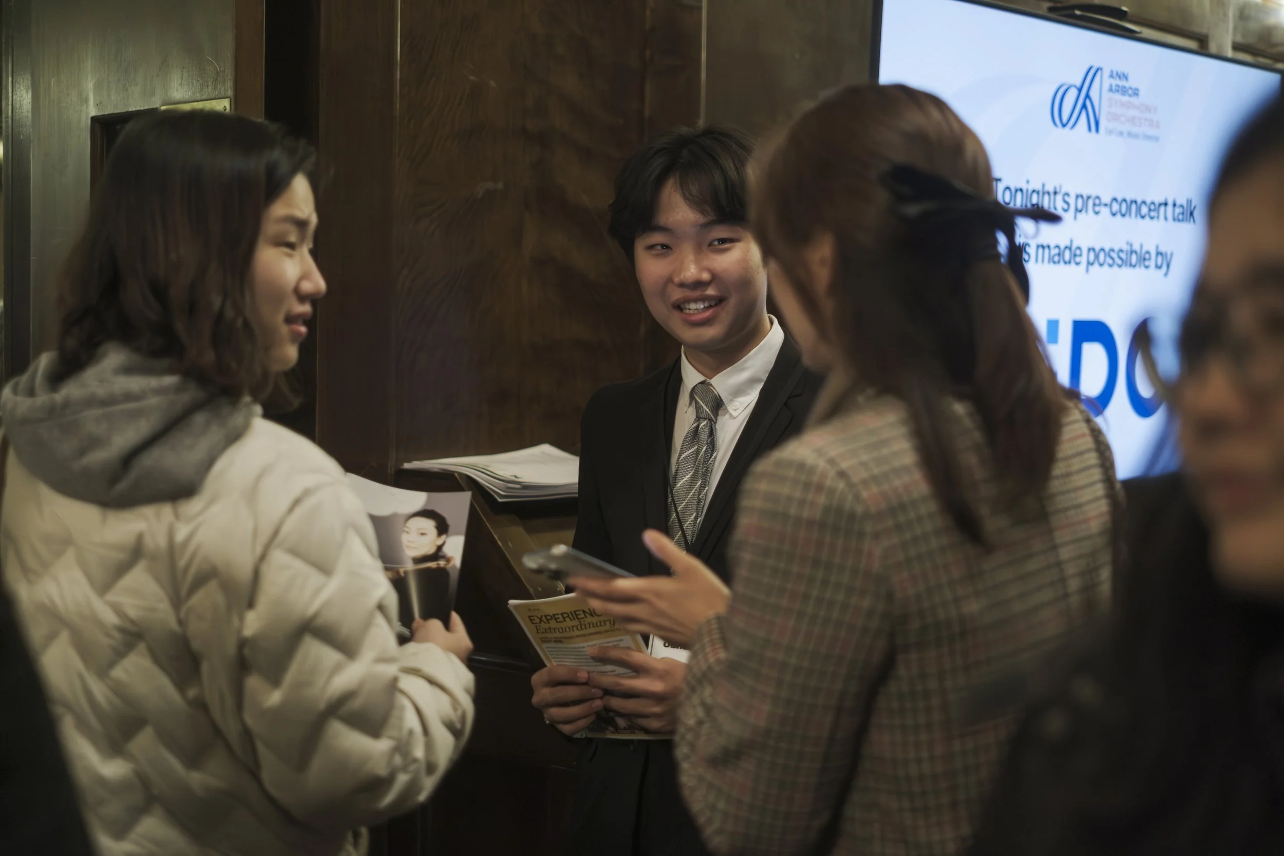 An Ann Arbor Symphony Orchestra staff member handing out brochures and interacting with people as they walk into the Michigan Theater.