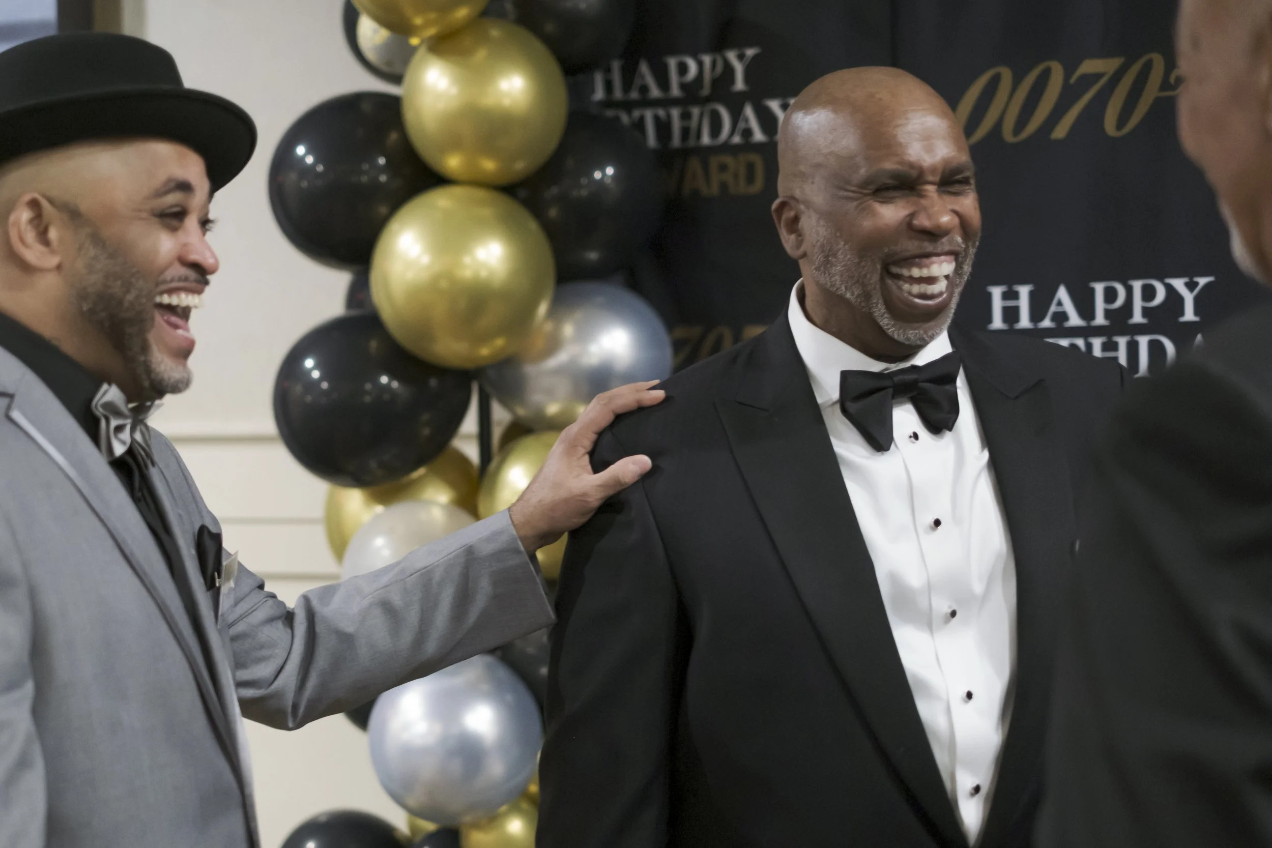 Two men laugh dressed in suits.