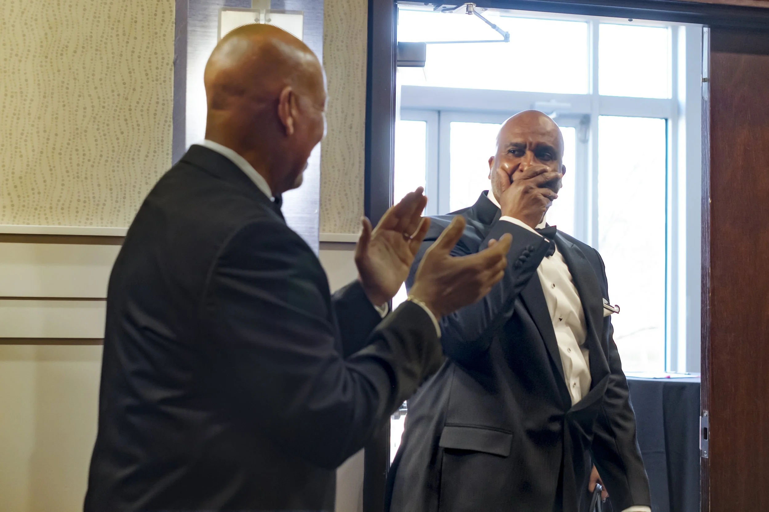 A man put his hand over his mouth with a surprised expression as another man claps.
