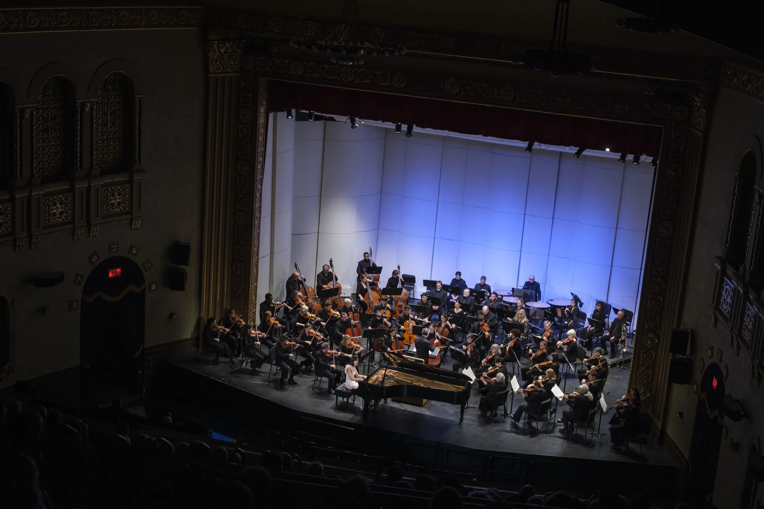 An orchestra on stage with a pianist near the front of the stage.