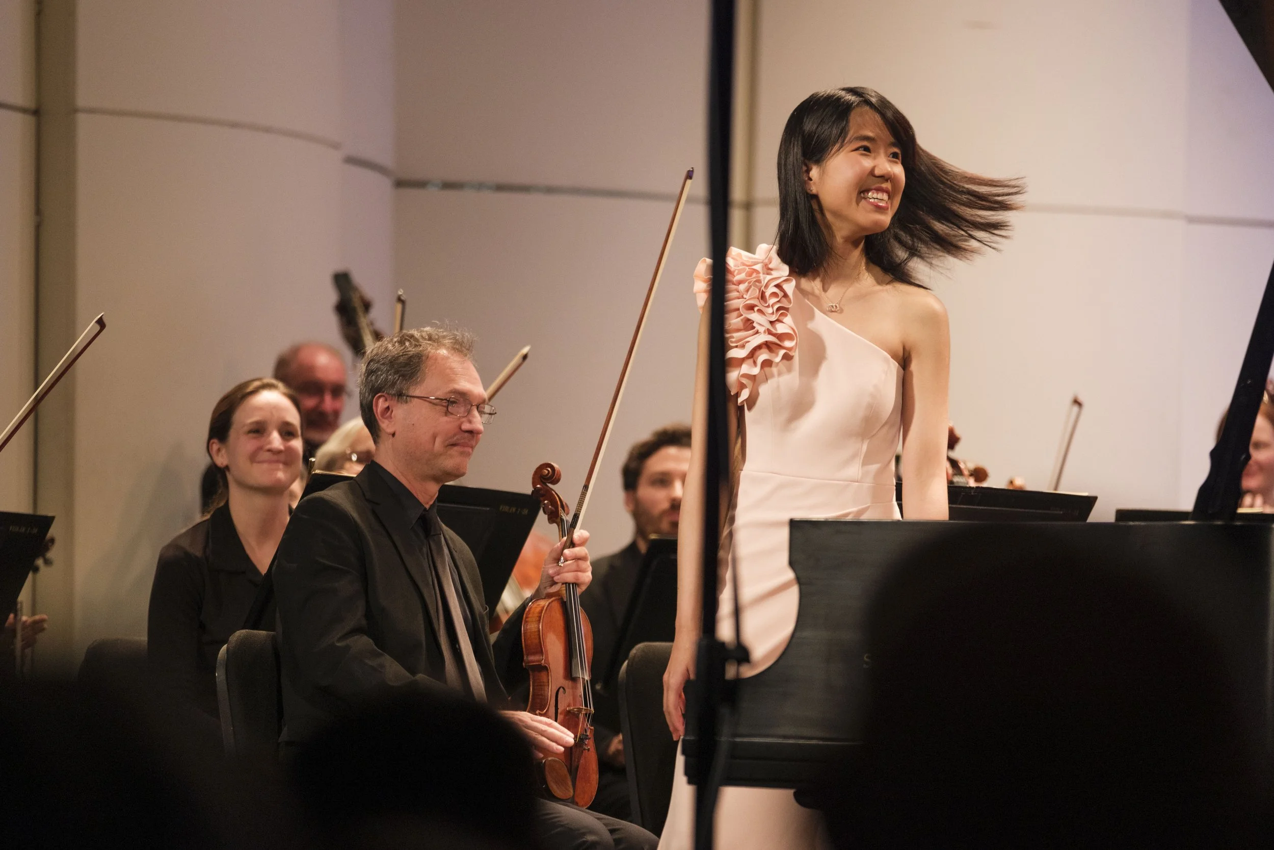 Pianist Kate Liu stands on stage smiling after performing a solo during a concert.