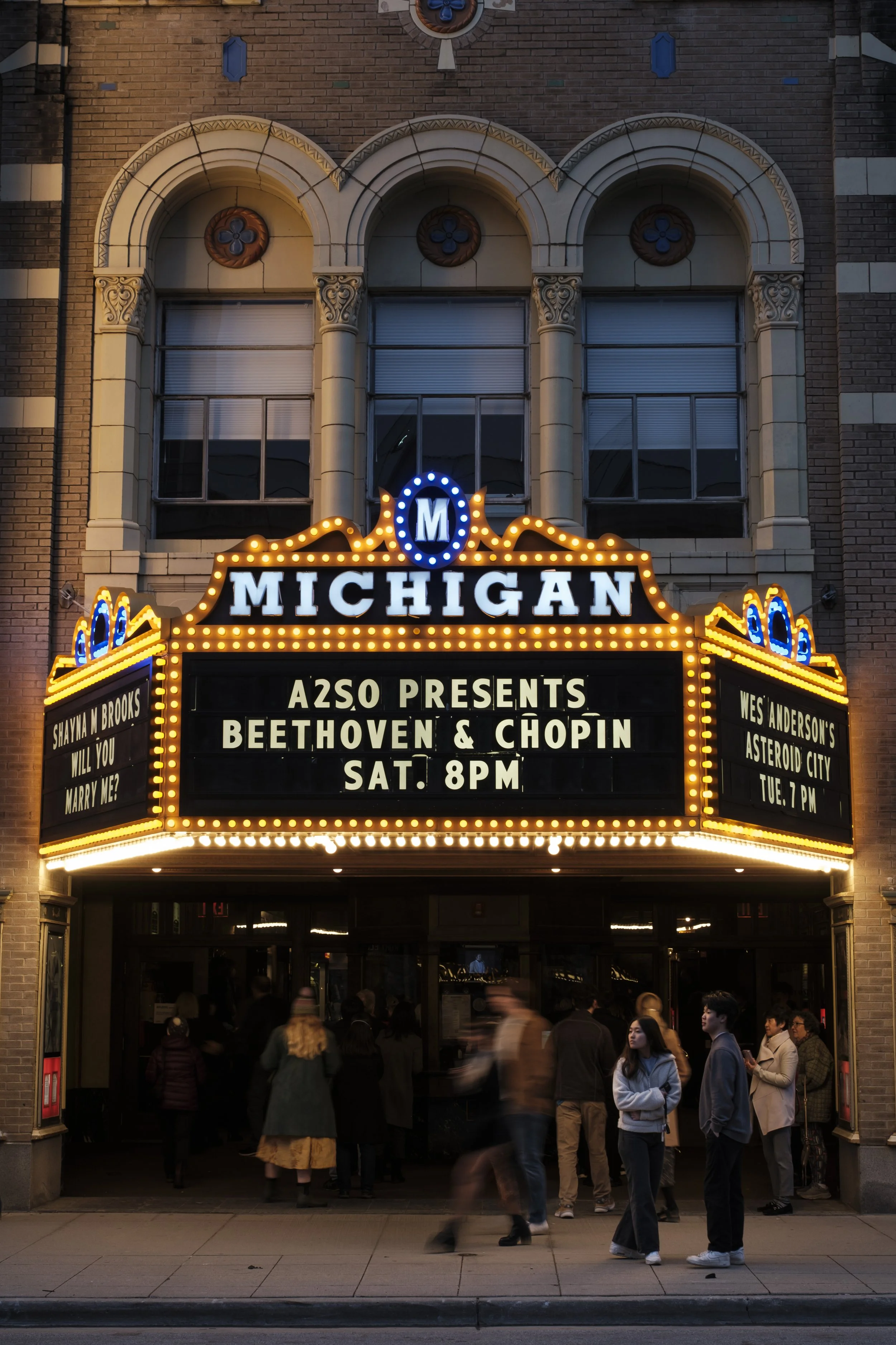 Blurry people move under a theater marquee.