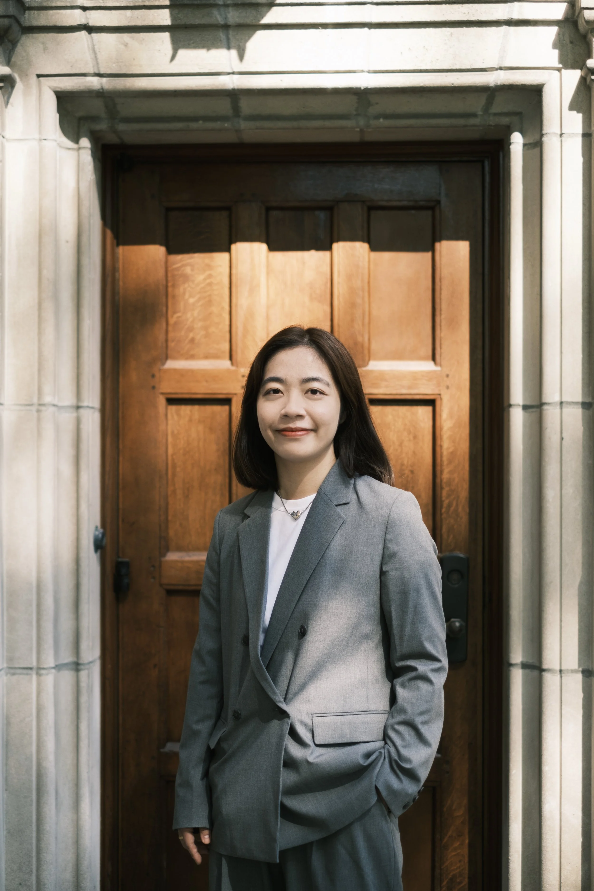 A person stands and smiles in a door way in a suit and is illuminated by sunlight.