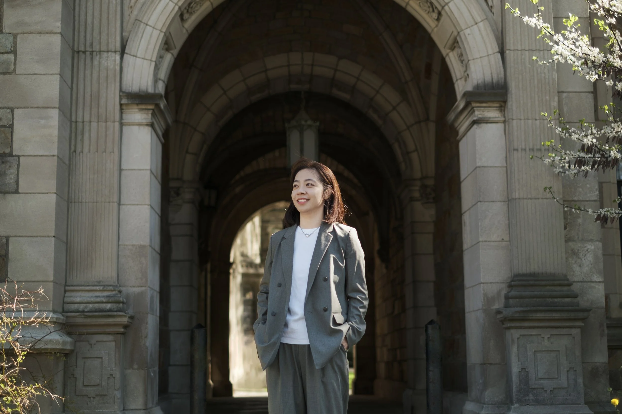 A person stands in front of a brick building, illuminated by sunlight on campus of the University of Michigan.
