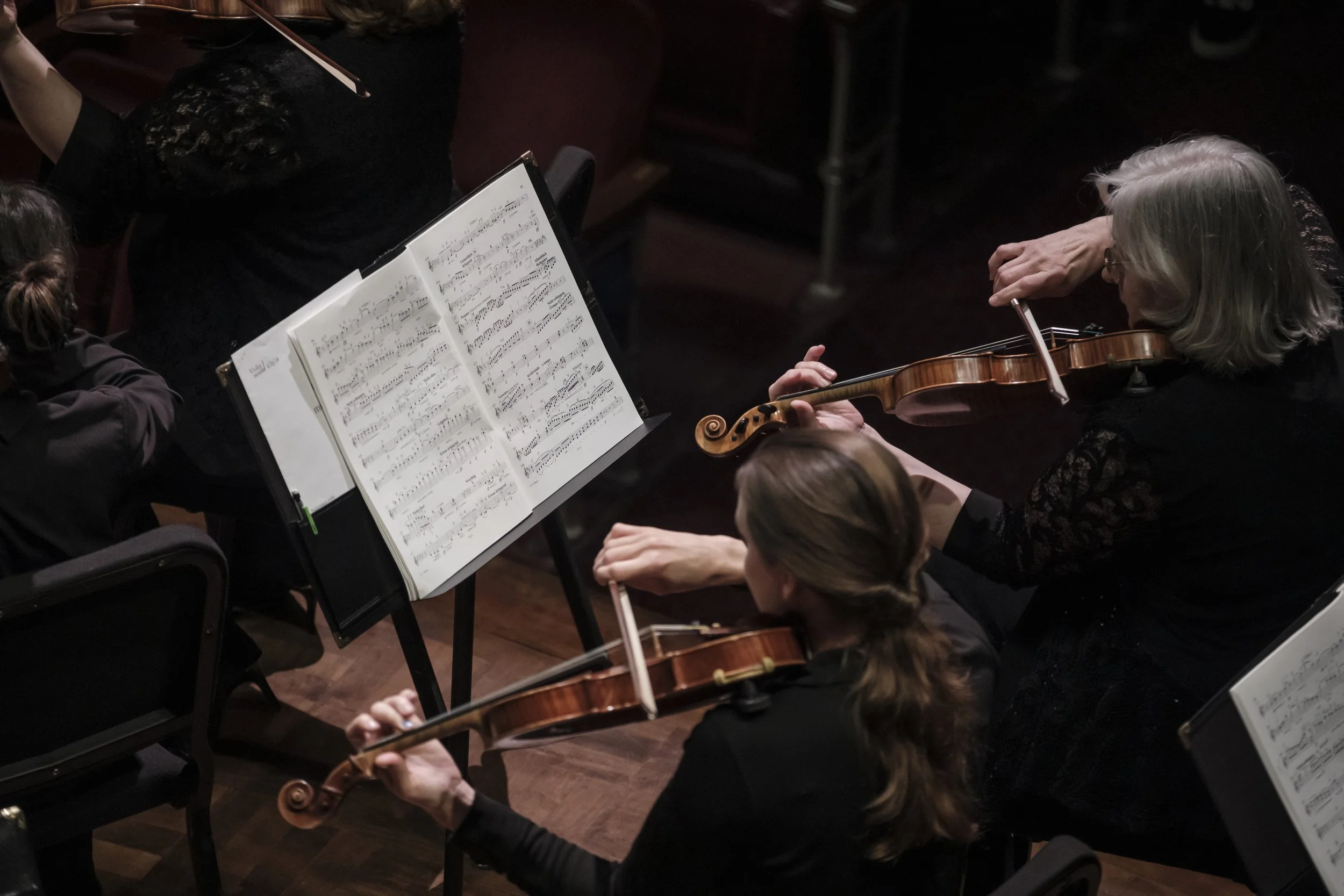 Musicians on stage holding violins and looking at sheet music during a concert.