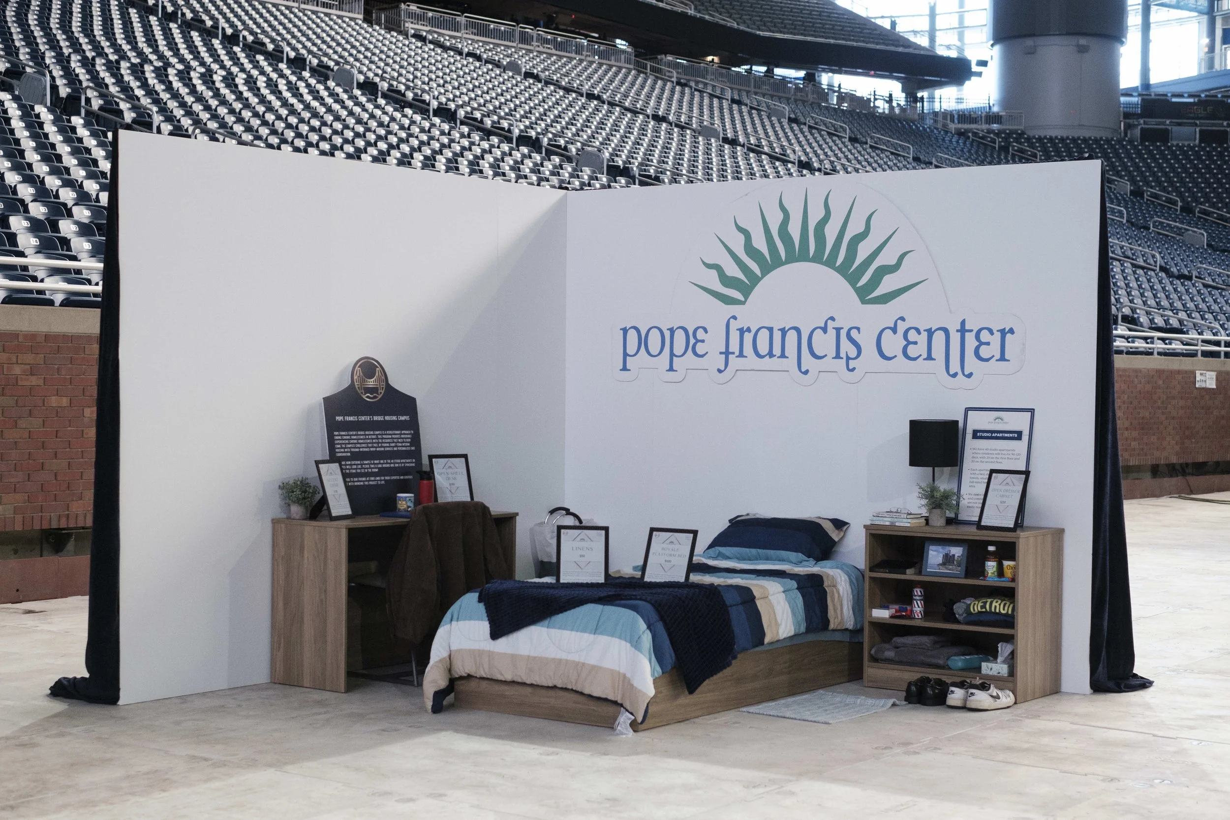 A room setup example display with a bed, shelves, and dresser in a stadium.