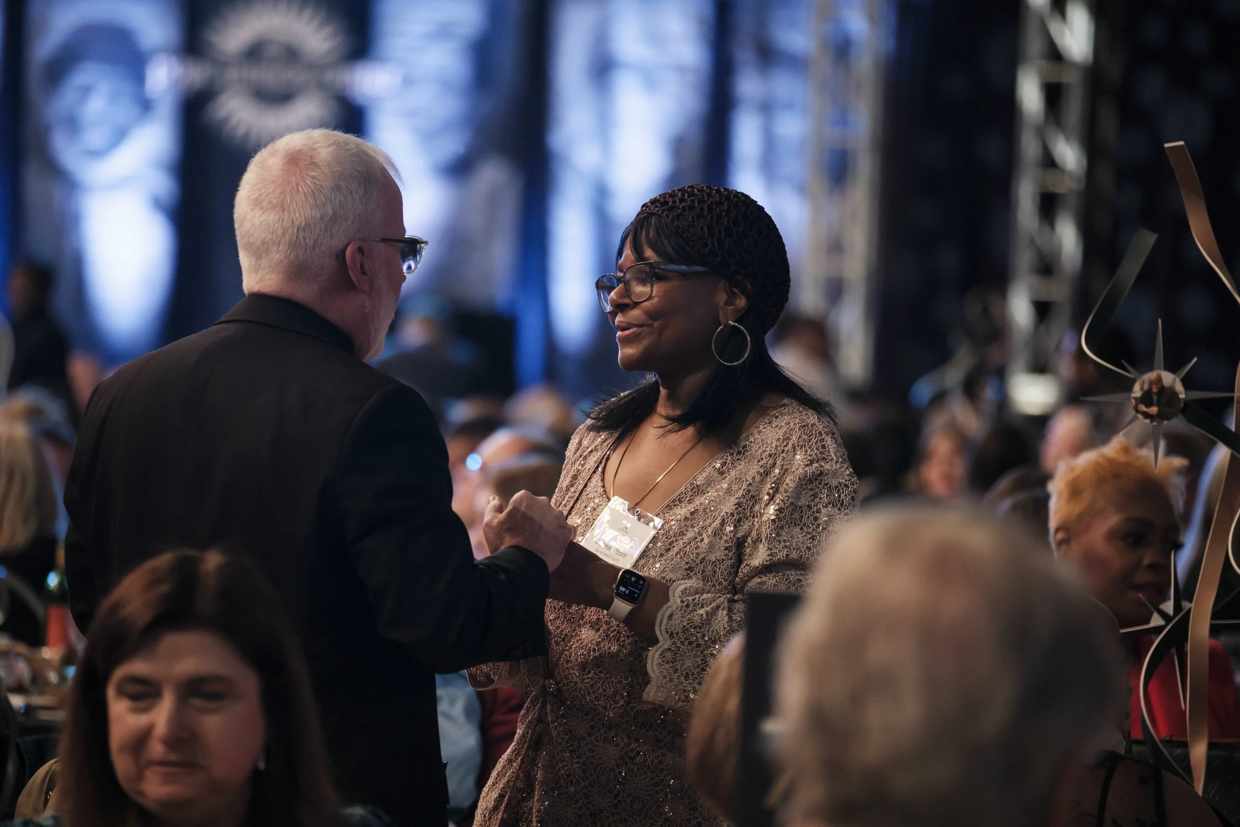 A man and a woman talk to one another in a crowd of people during a gala event.
