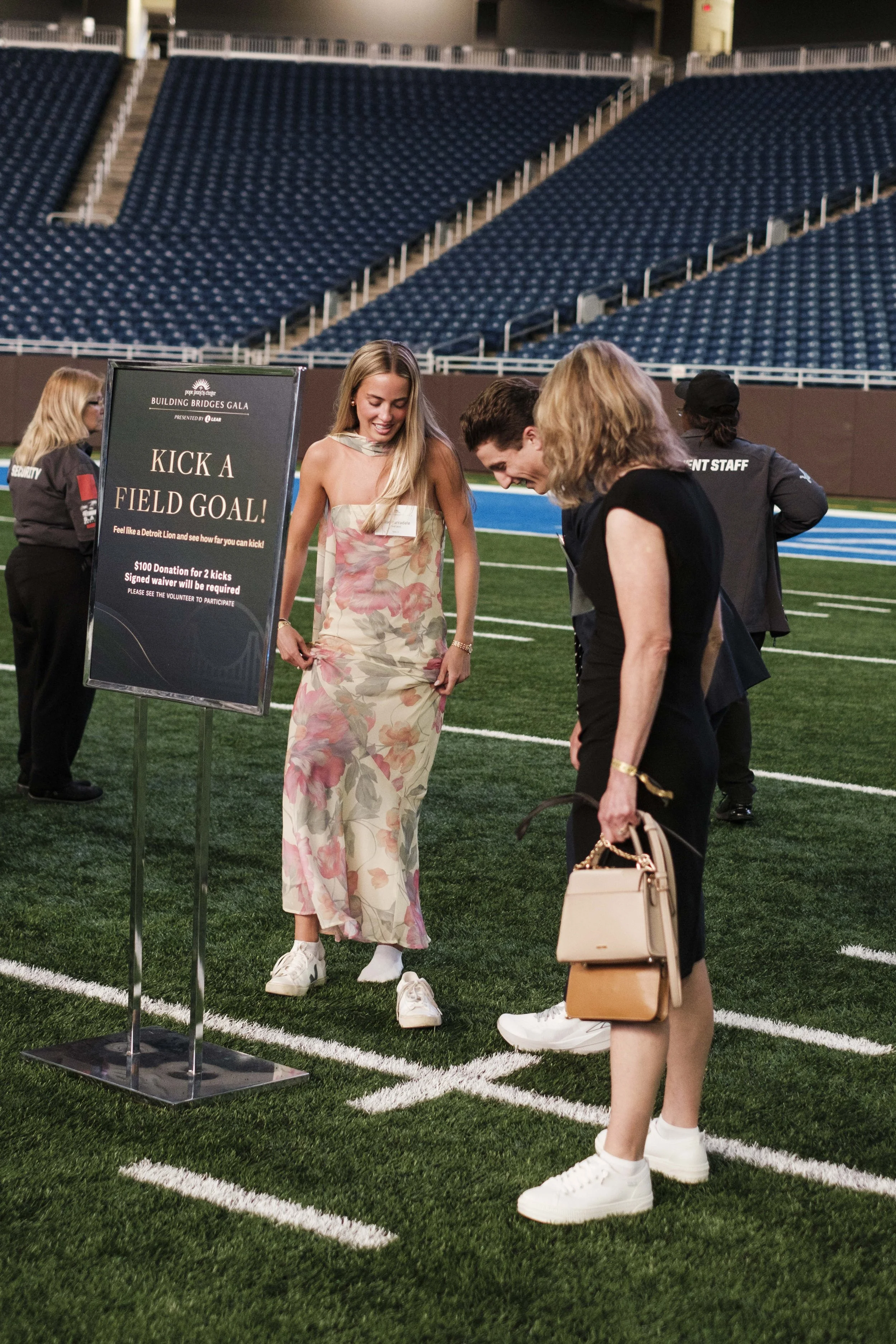 A woman wearing a dress put on tennis shoes on a football field.