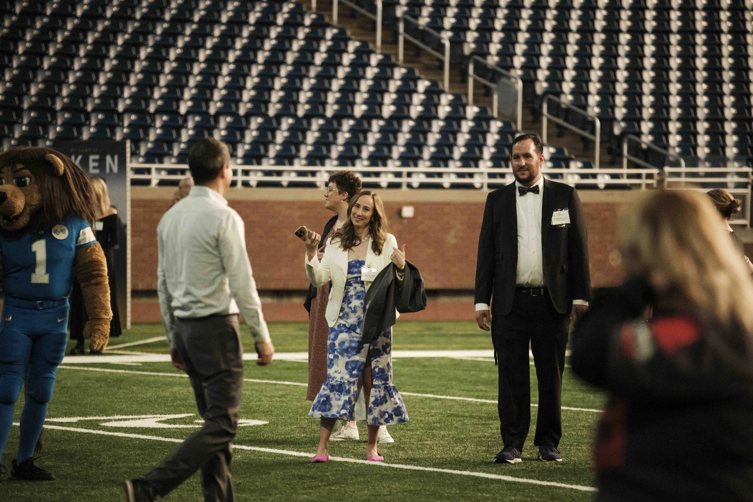 A woman gives a thumbs up to a man in a crowd while standing on a football field.