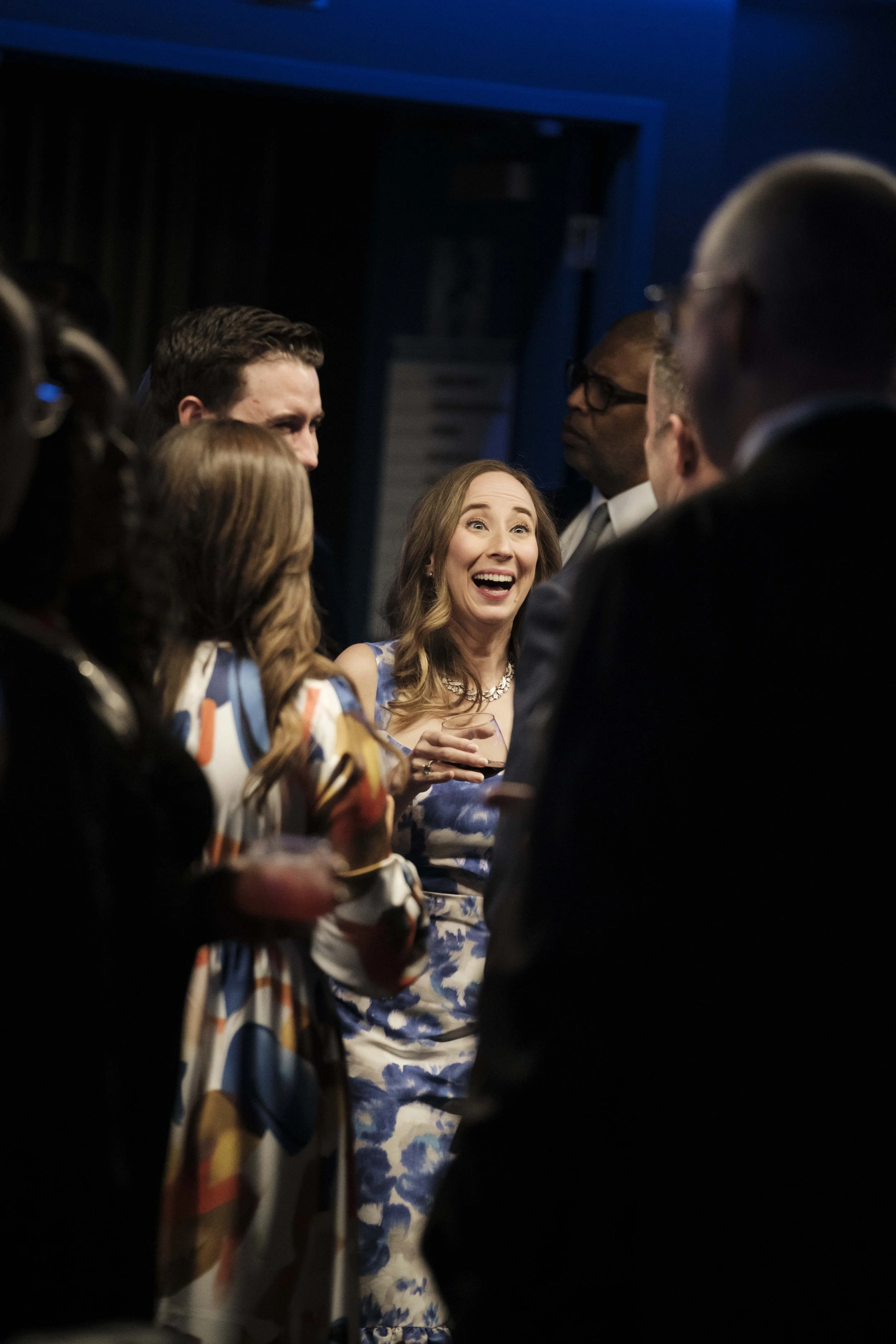 A woman smiles and laughs while talking to another person while in a crowd of people during a gala event.