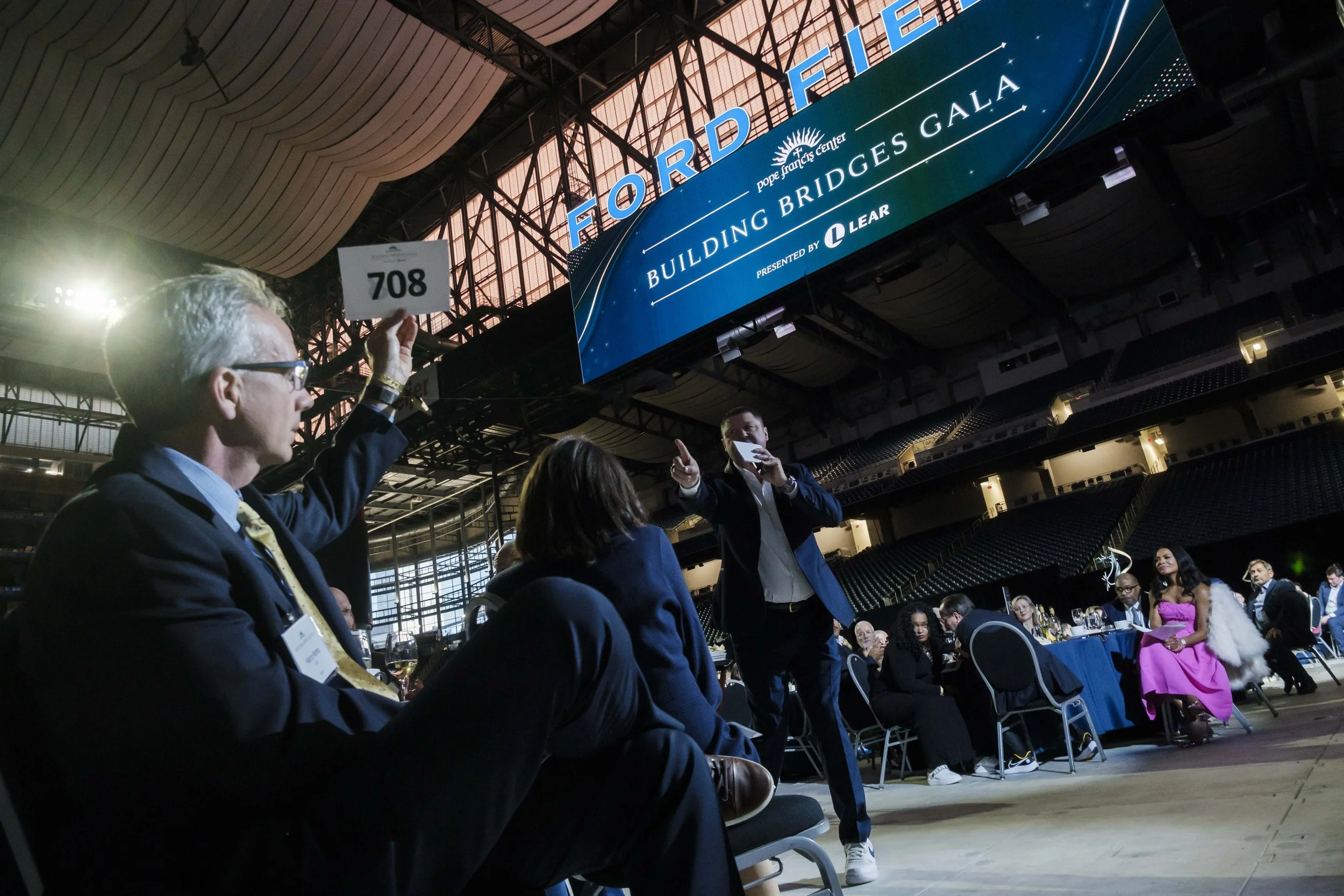 A man holds up a piece of paper with a number on it while another man holding a microphone points at it.