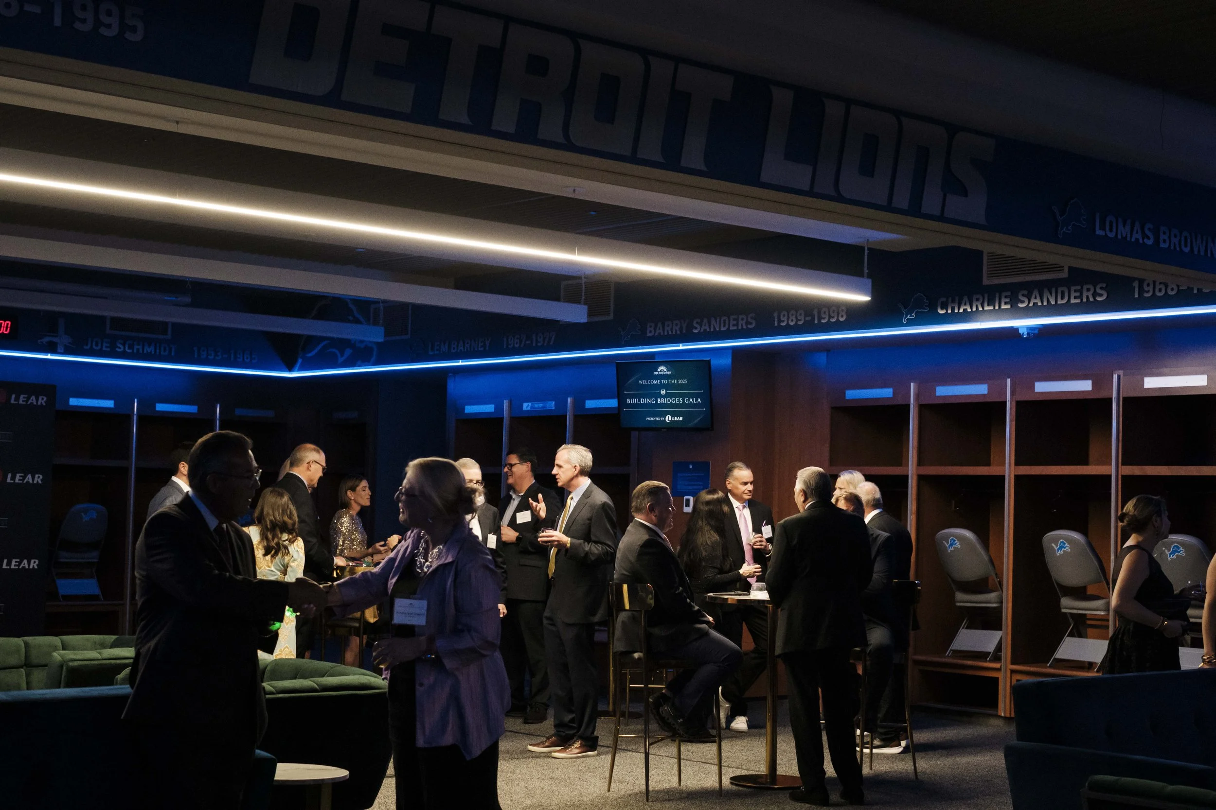 A crowd of people sit and talk while illuminated by overhead lighting.