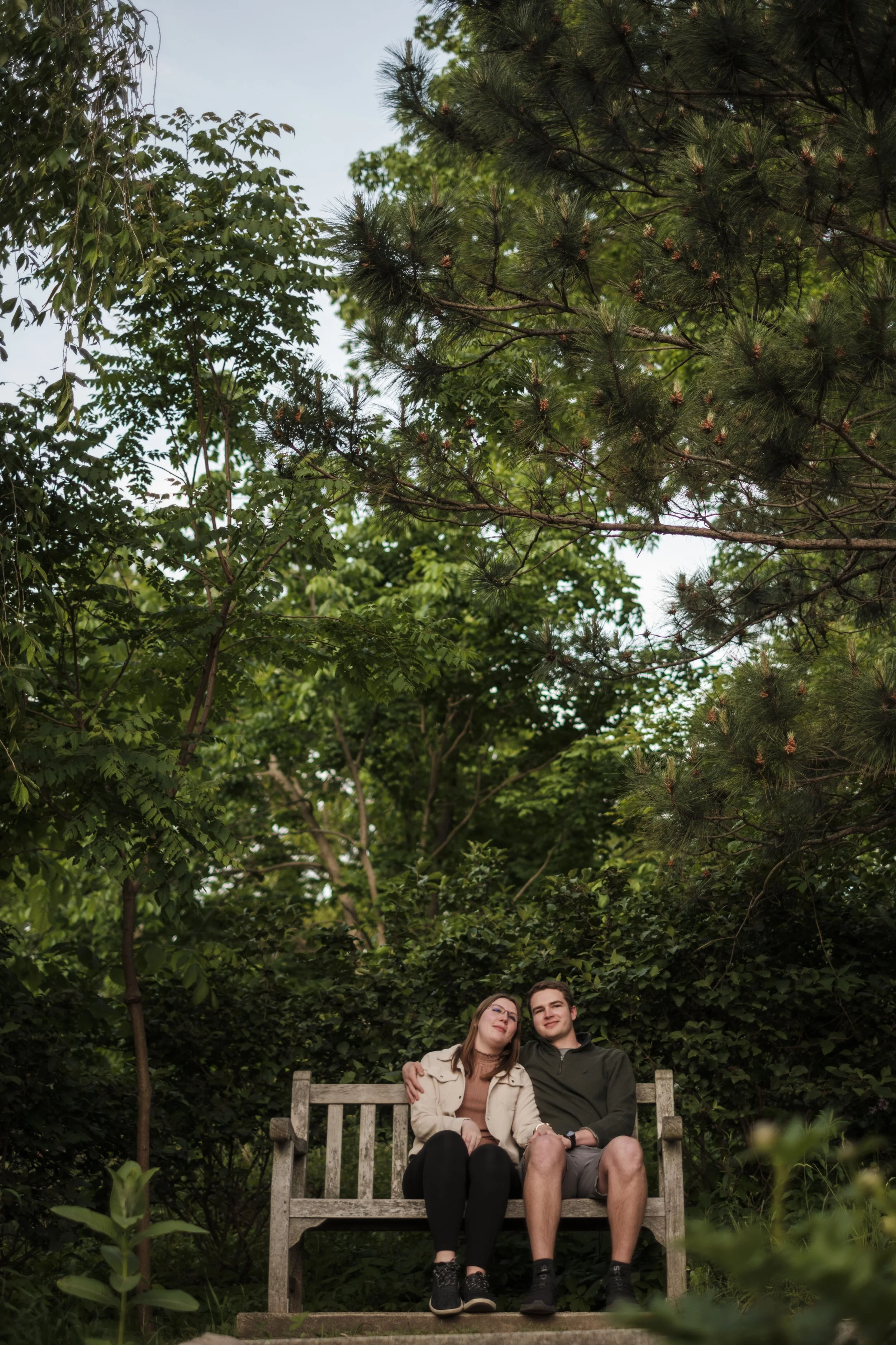 A couple sits on a bench surrounded by trees at Nichols Arb in Ann Arbor.